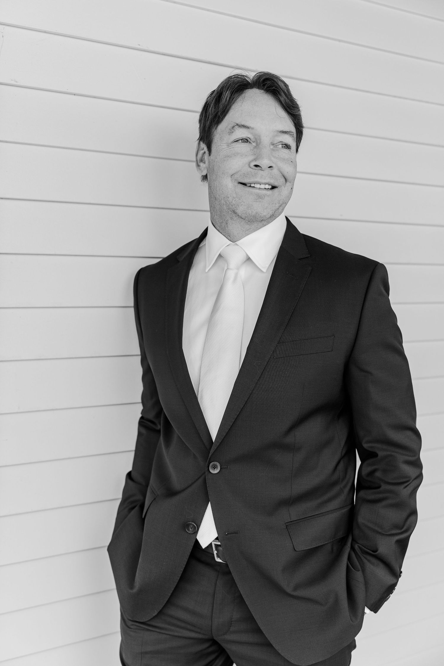 Black and white portrait of a person in formal attire against white siding.