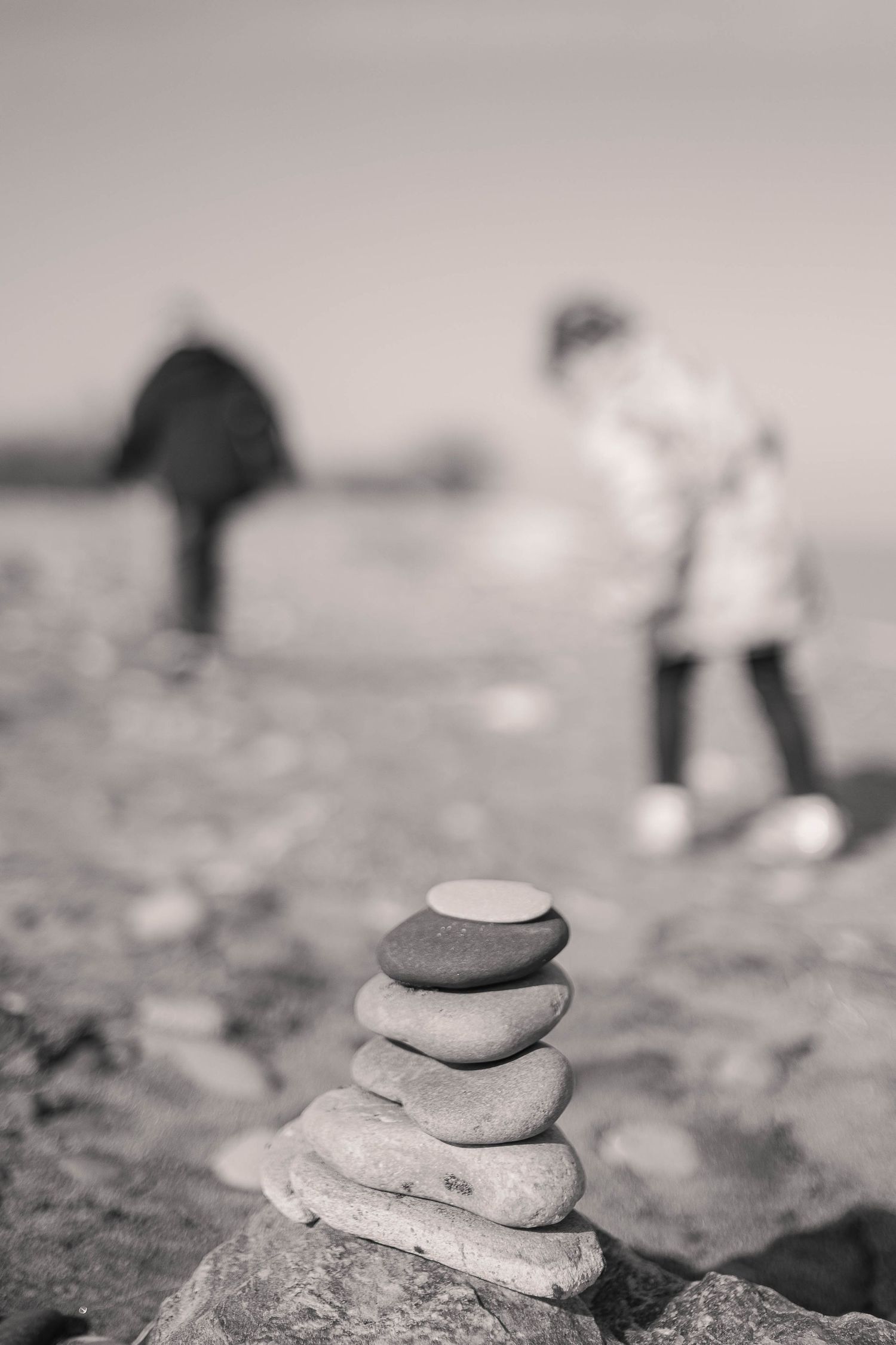 Black and white image of stacked stones with blurred figures in background.