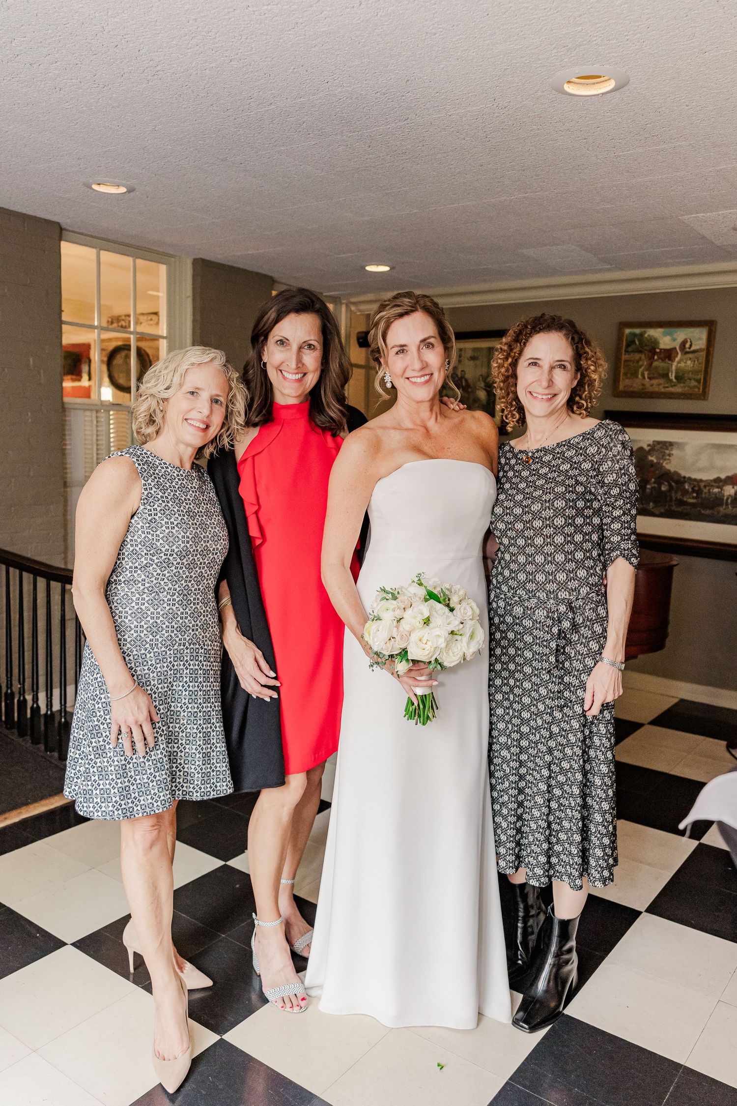 Group photo of wedding party members in formal attire on black and white checkered floor.