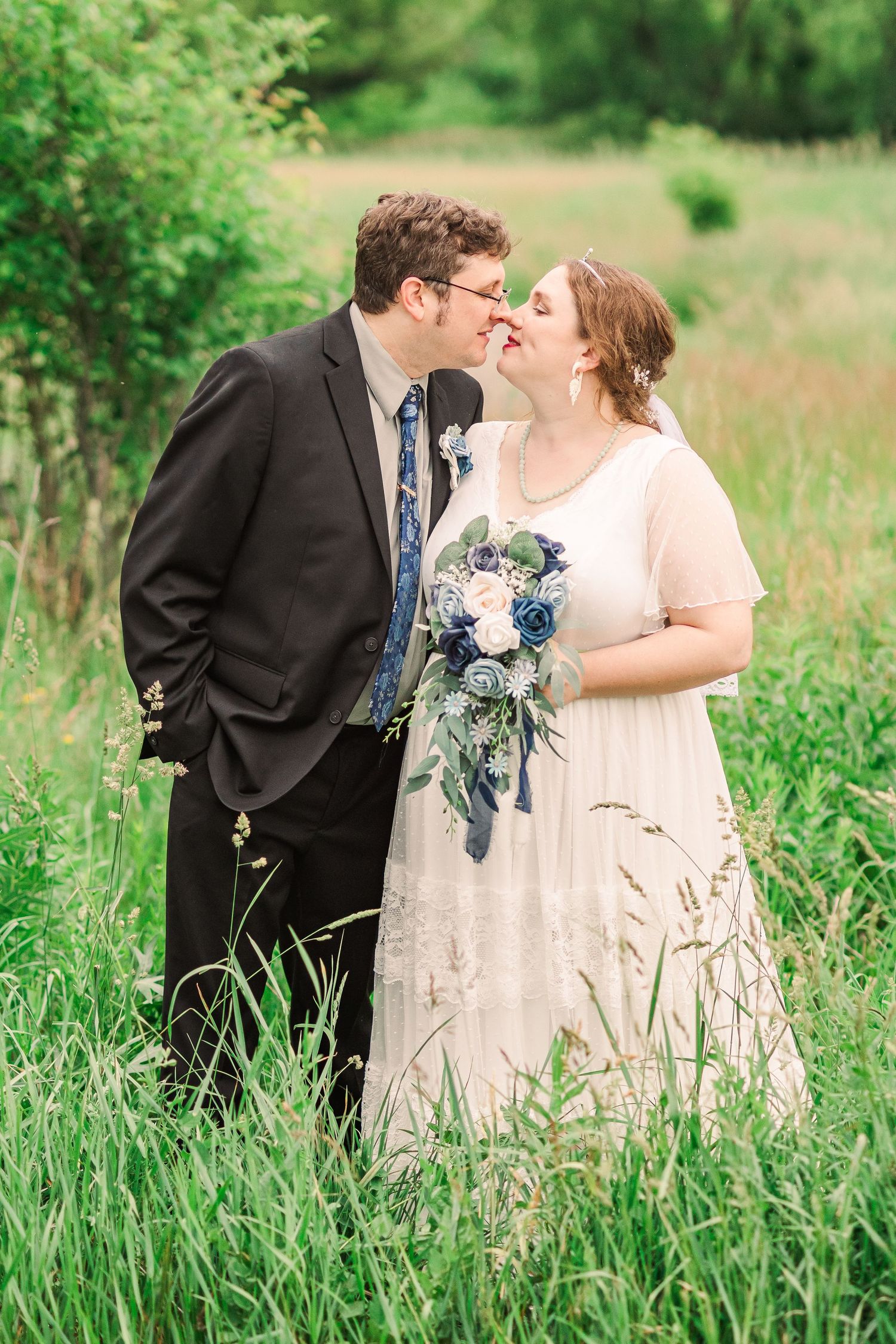 Romantic wedding portrait surrounded by tall grass in natural outdoor setting.