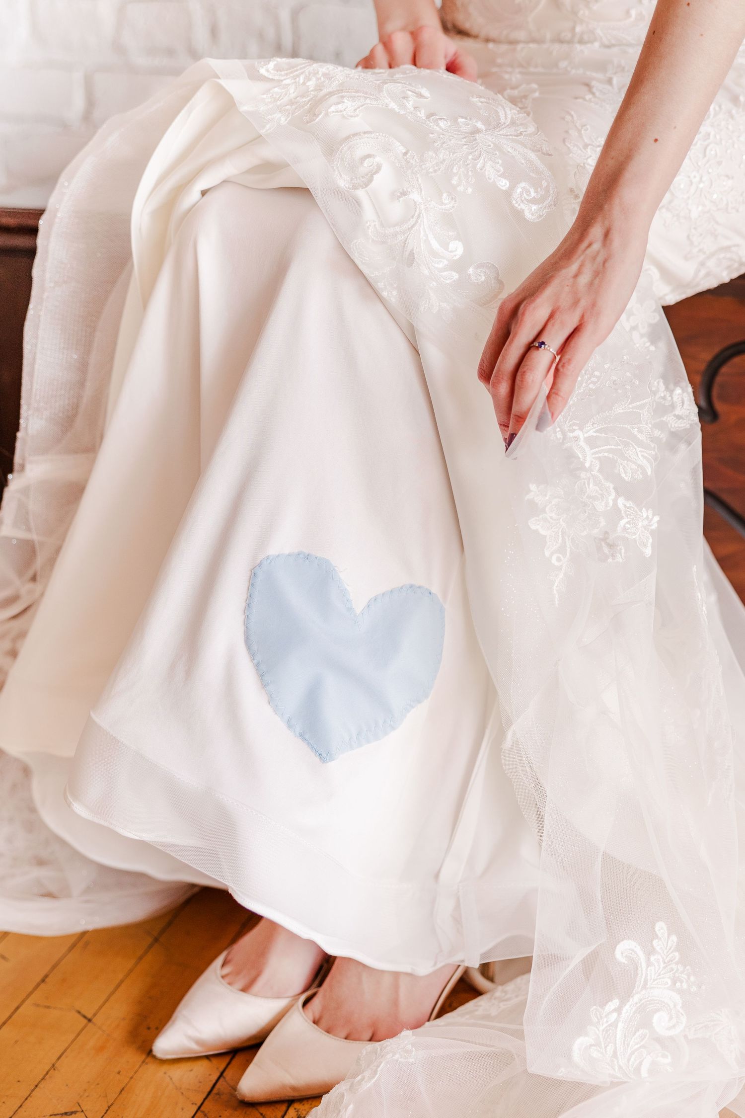 Wedding dress detail showing blue heart patch with lace embellishments and white shoes.
