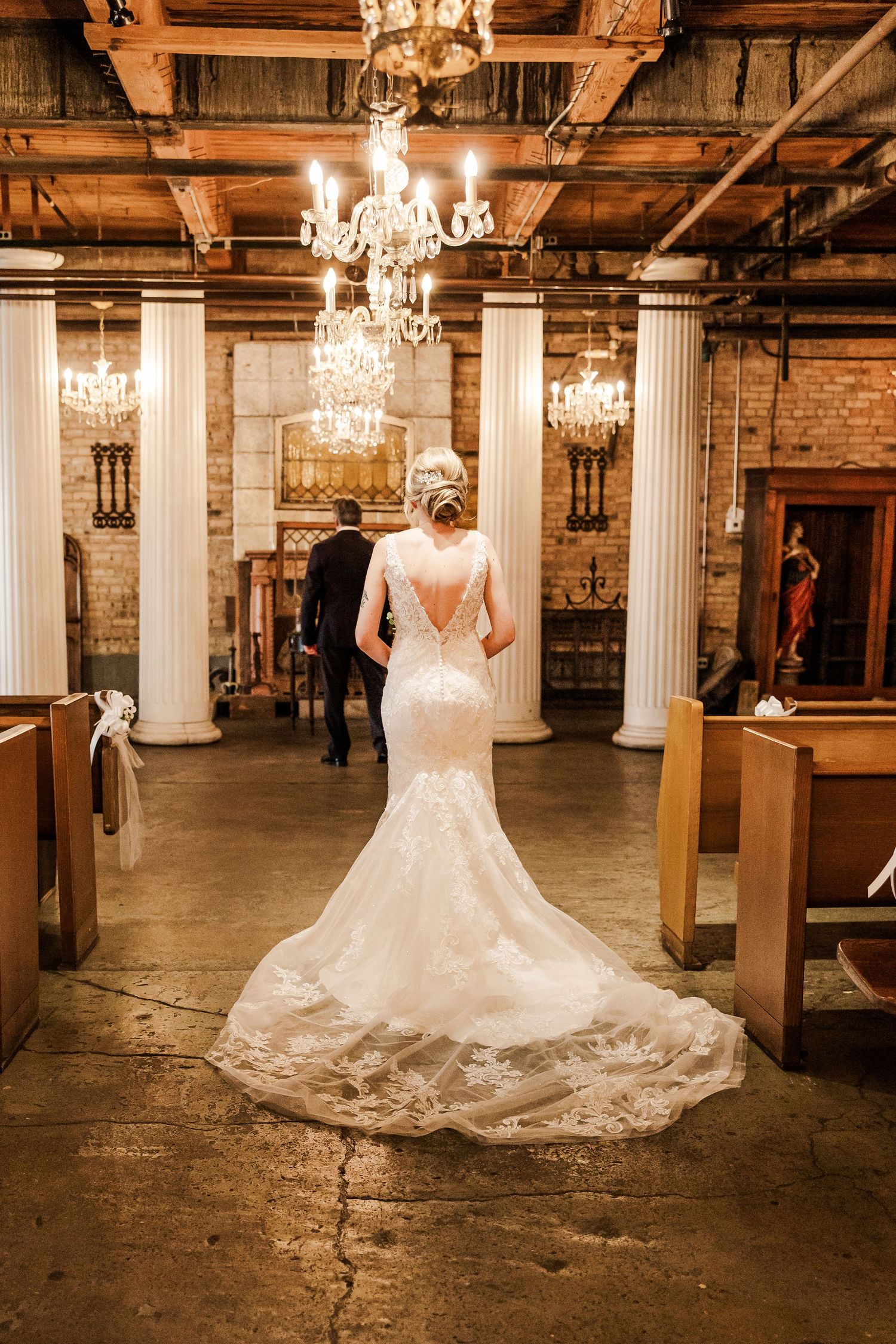 A warm-toned photo capturing a wedding dress silhouette against vintage brick walls and crystal chandeliers.