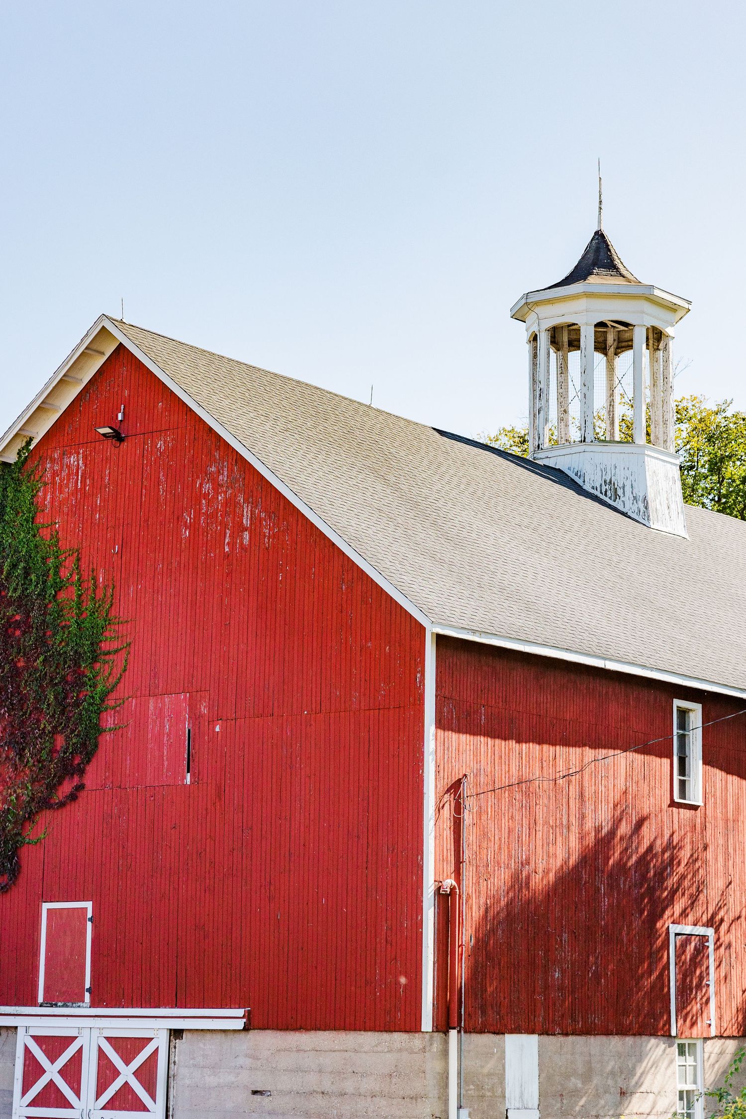 Classic red barn with white cupola and trim against blue sky.