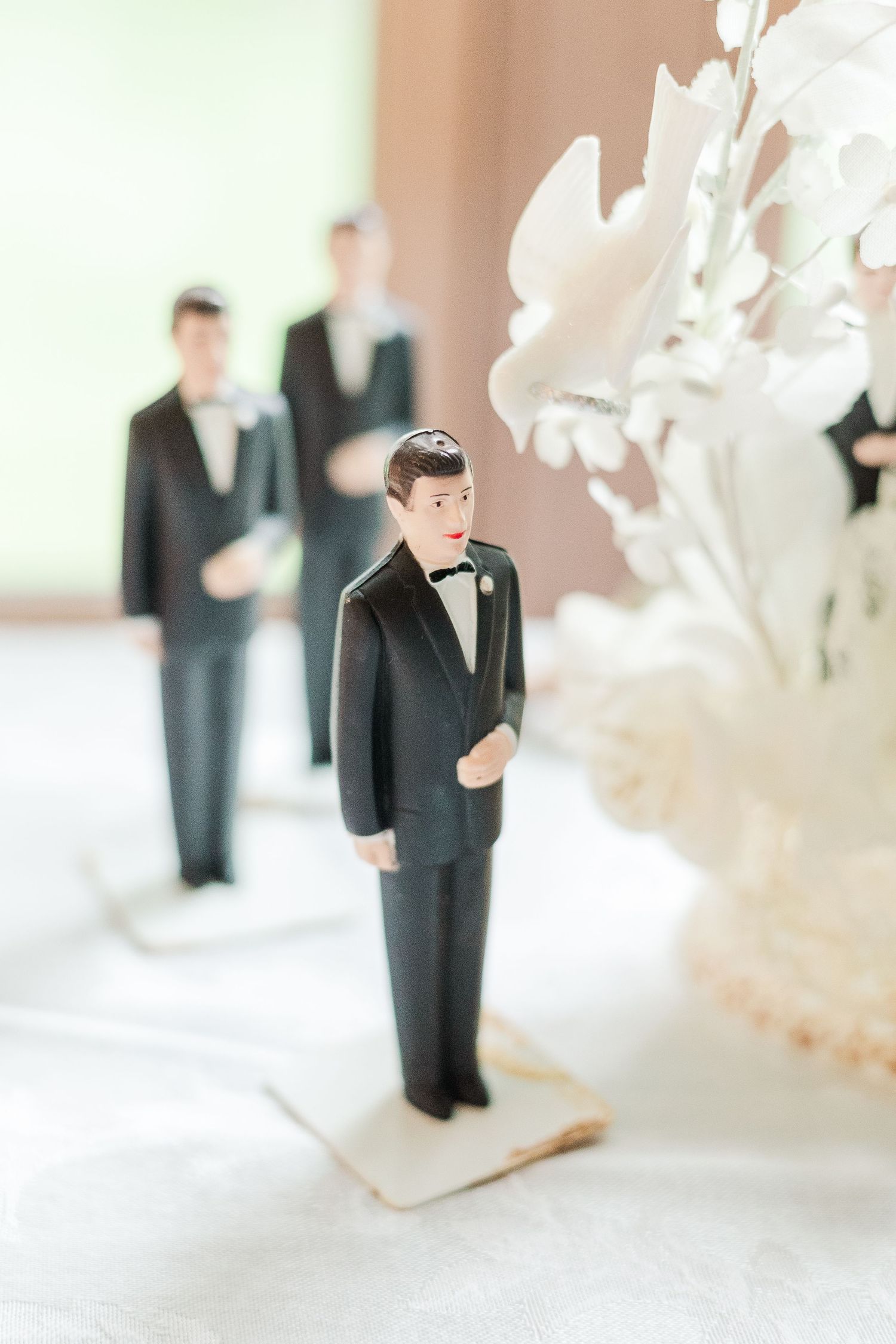 Small decorative wedding cake topper figurine in a tuxedo next to white floral decor.