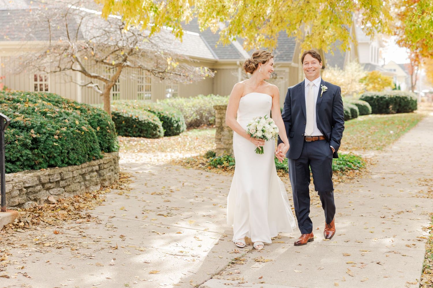 A candid wedding moment captured on a leaf-covered pathway in fall.
