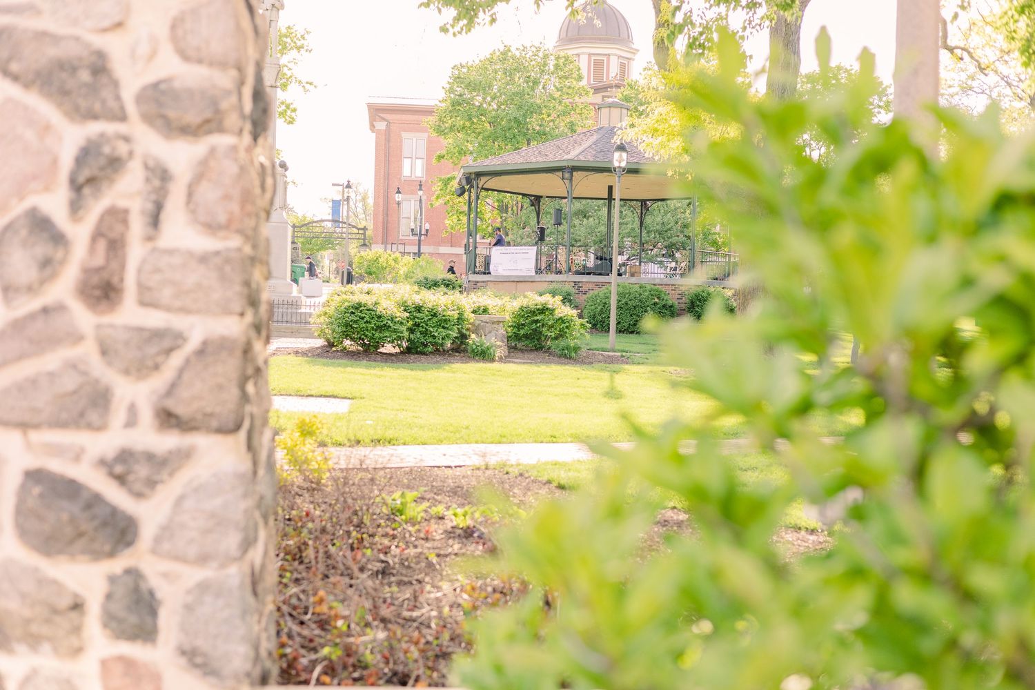 Scenic park pathway with gazebo, landscaping and historic buildings in background.