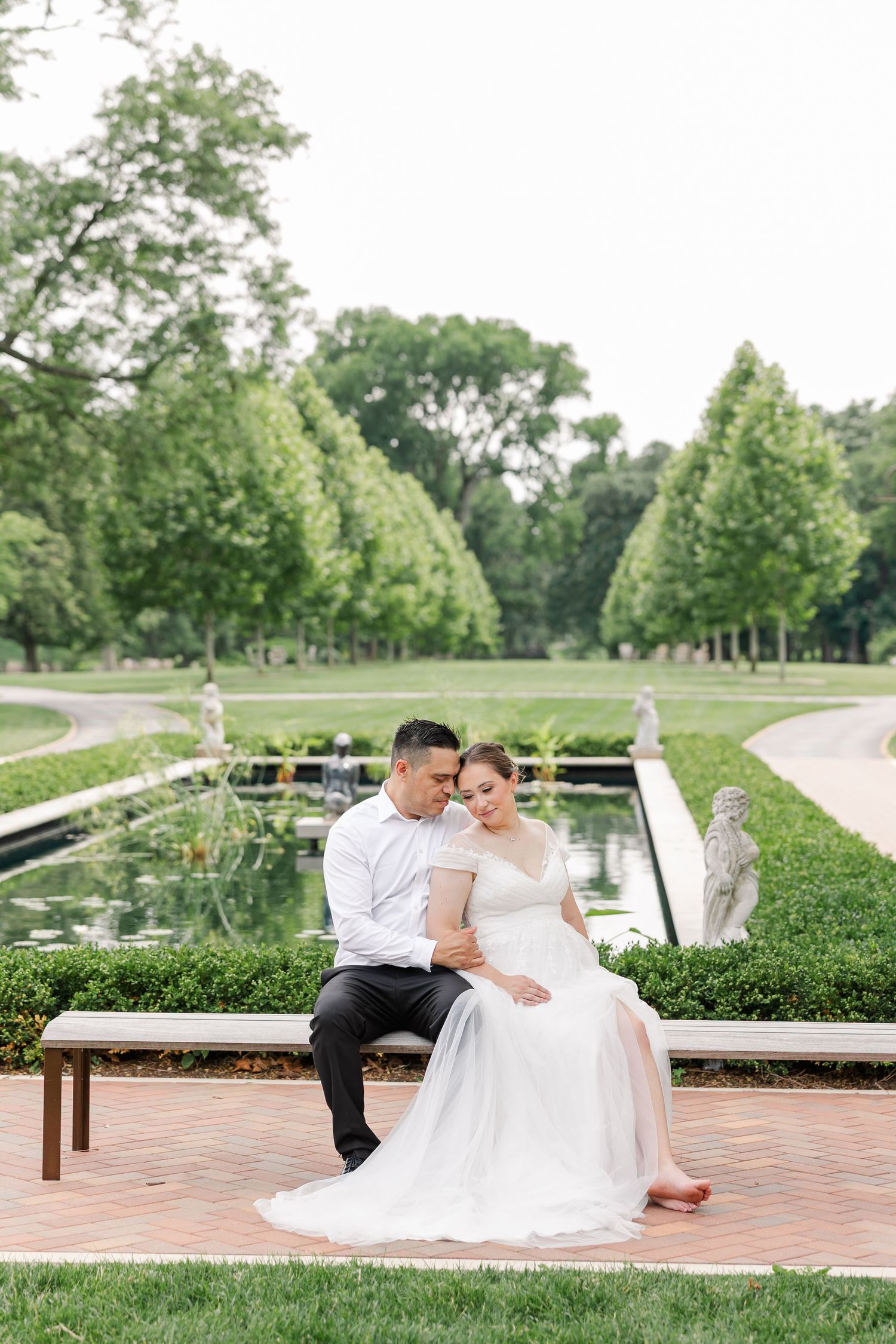 Monika and Rafael sharing a kiss while seated on a bench overlooking the gardens at Cantigny Park.