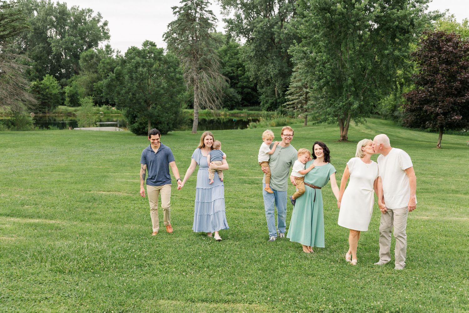 Extended family of seven walks together on green lawn surrounded by lush trees.
