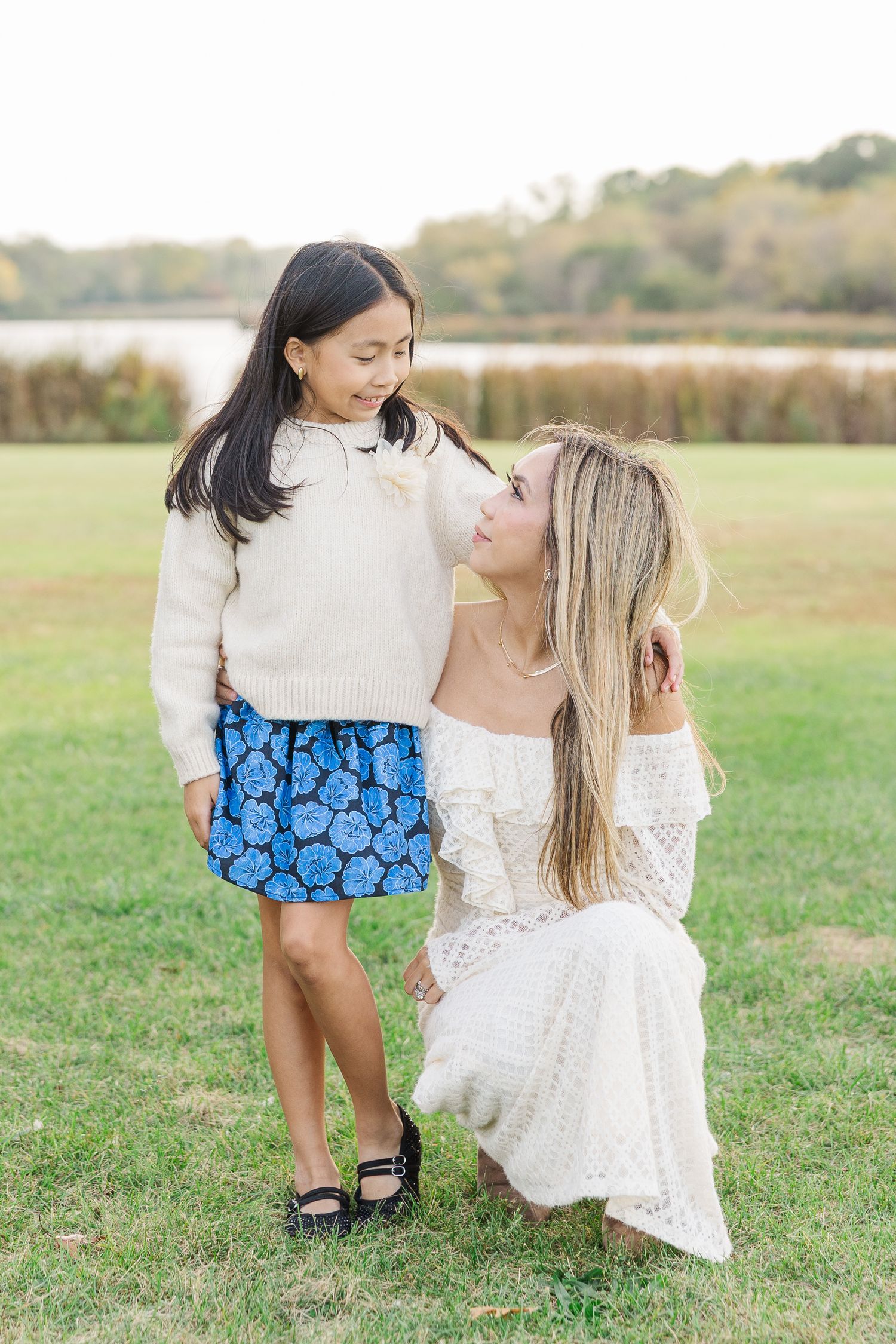 Two people in coordinating outfits pose together playfully in a grassy field during a photo session. Busse Woods
