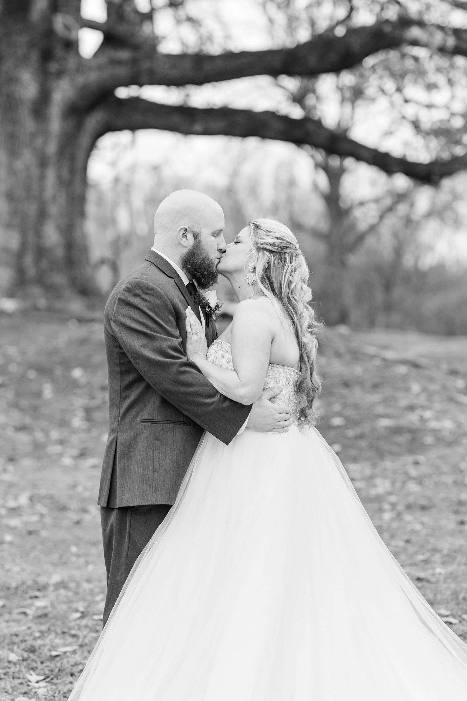 A romantic black and white wedding portrait captured under towering trees.