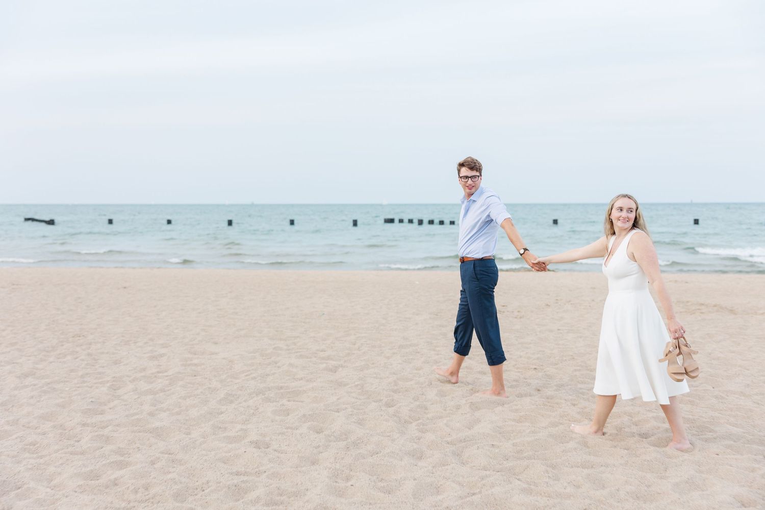 Elizabeth and Joe walking hand-in-hand along North Avenue Beach, with gentle waves and a soft sunset in the background