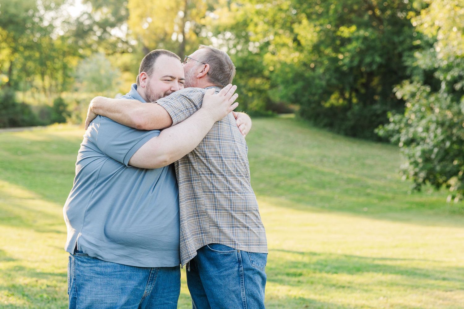 Two people share affectionate side hugs while standing in a sunlit green park during golden hour. Sorg family portraits at Shamrock Hills