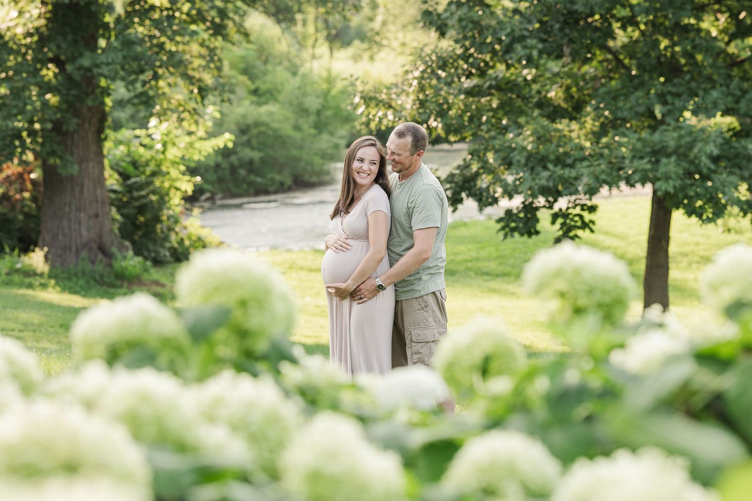 Couple standing together among blooming white hydrangea bushes in a sunlit garden path.