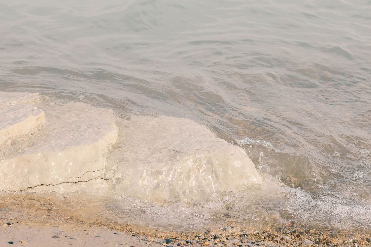 Close-up view of shallow waves washing over a sandy limestone shoreline.