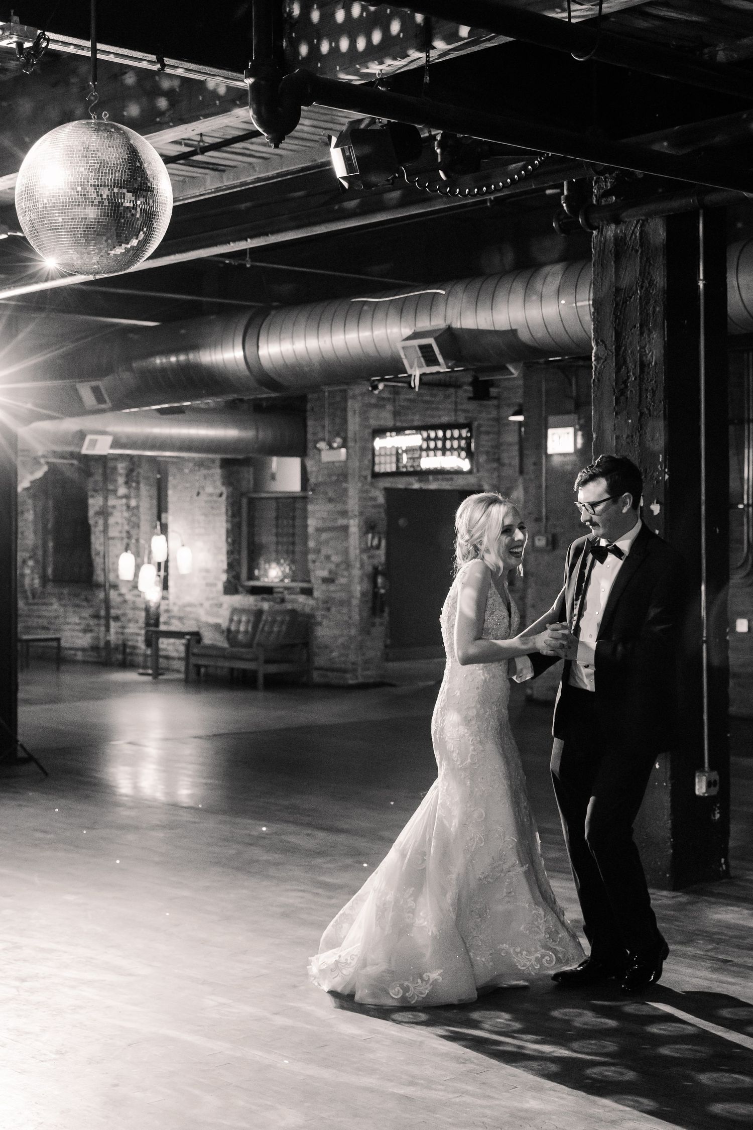 A black and white photo of a wedding dance under a disco ball in an urban industrial space.
