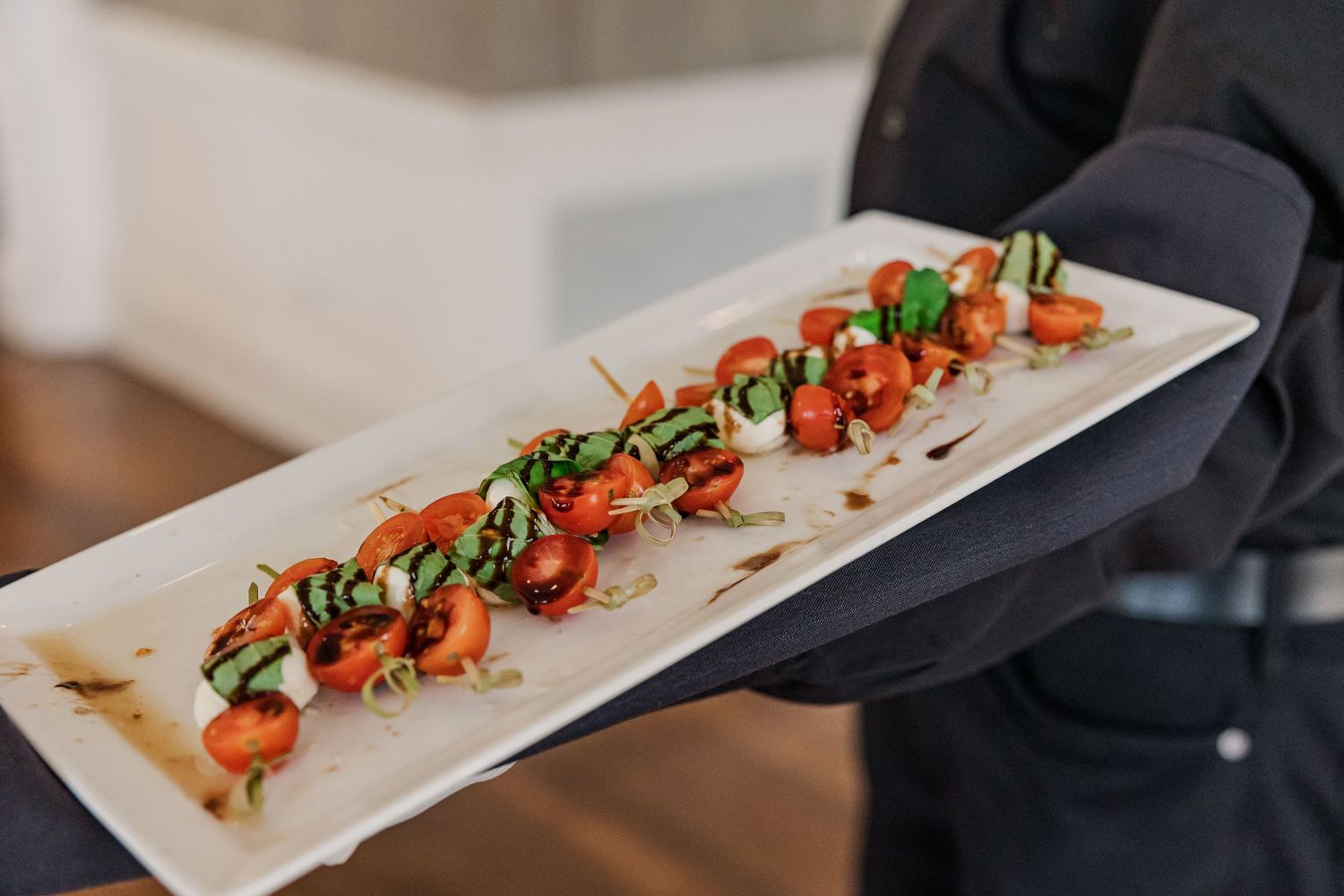 Beautifully plated appetizers with tomatoes and herbs served on a long white dish.