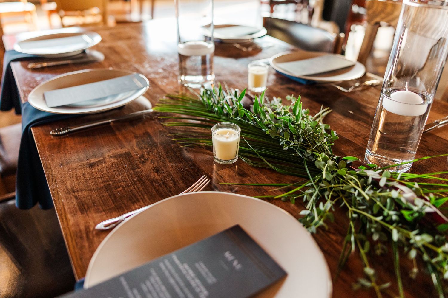 Wedding reception table setting with white plates, menus and fresh greenery garland.
