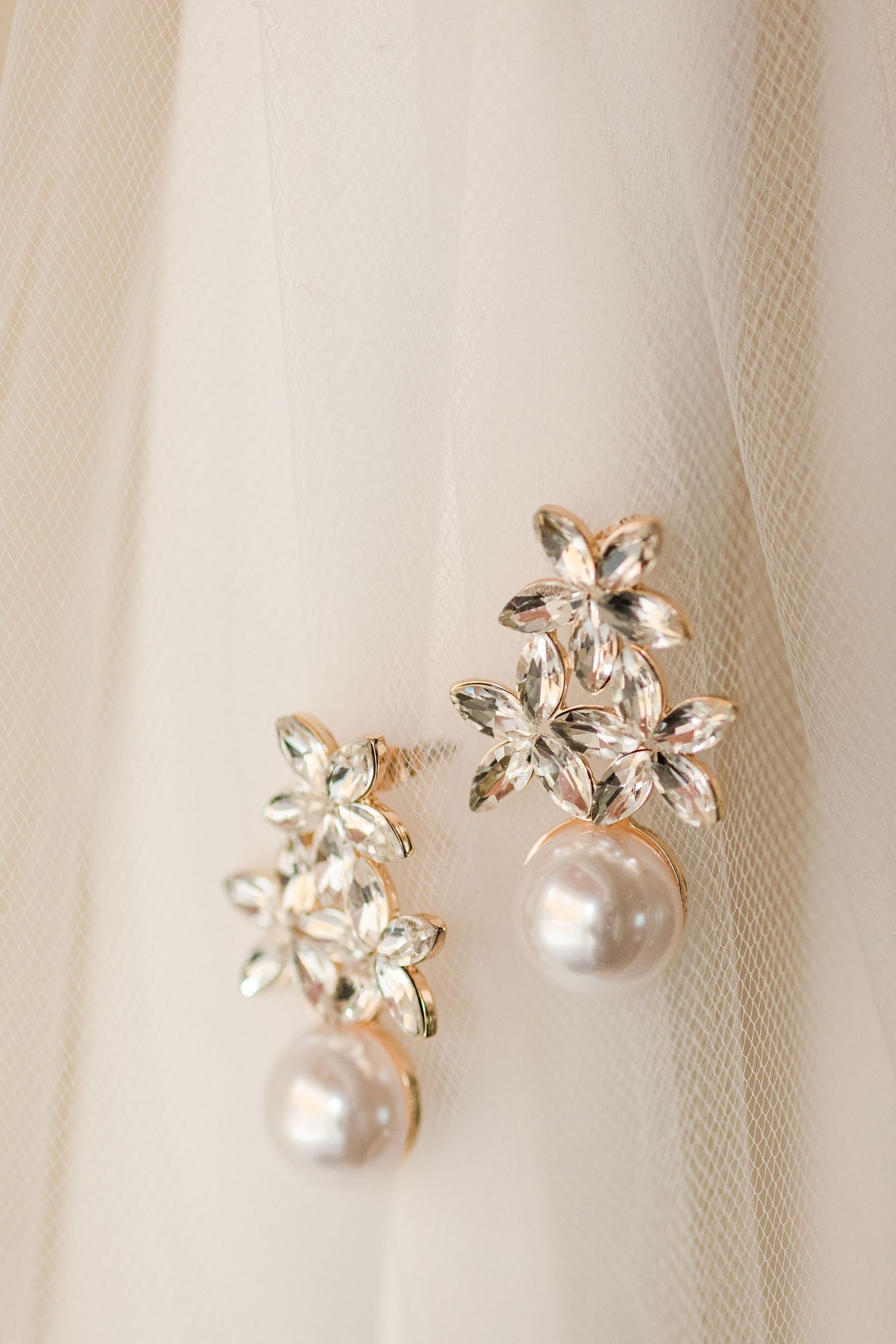 Delicate pearl and crystal flower earrings displayed on white tulle fabric.