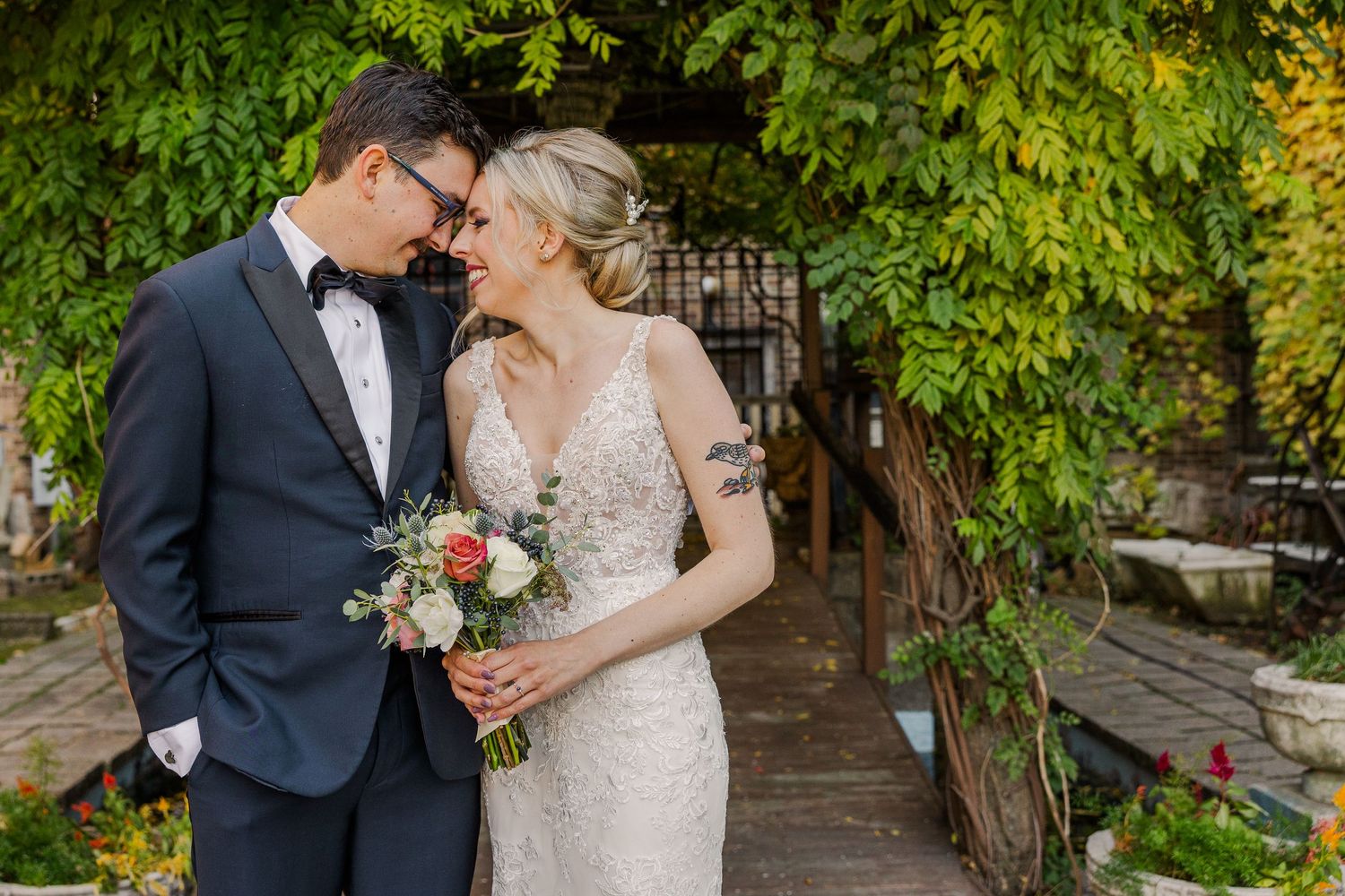 Intimate garden wedding portrait with couple sharing tender moment among green foliage.