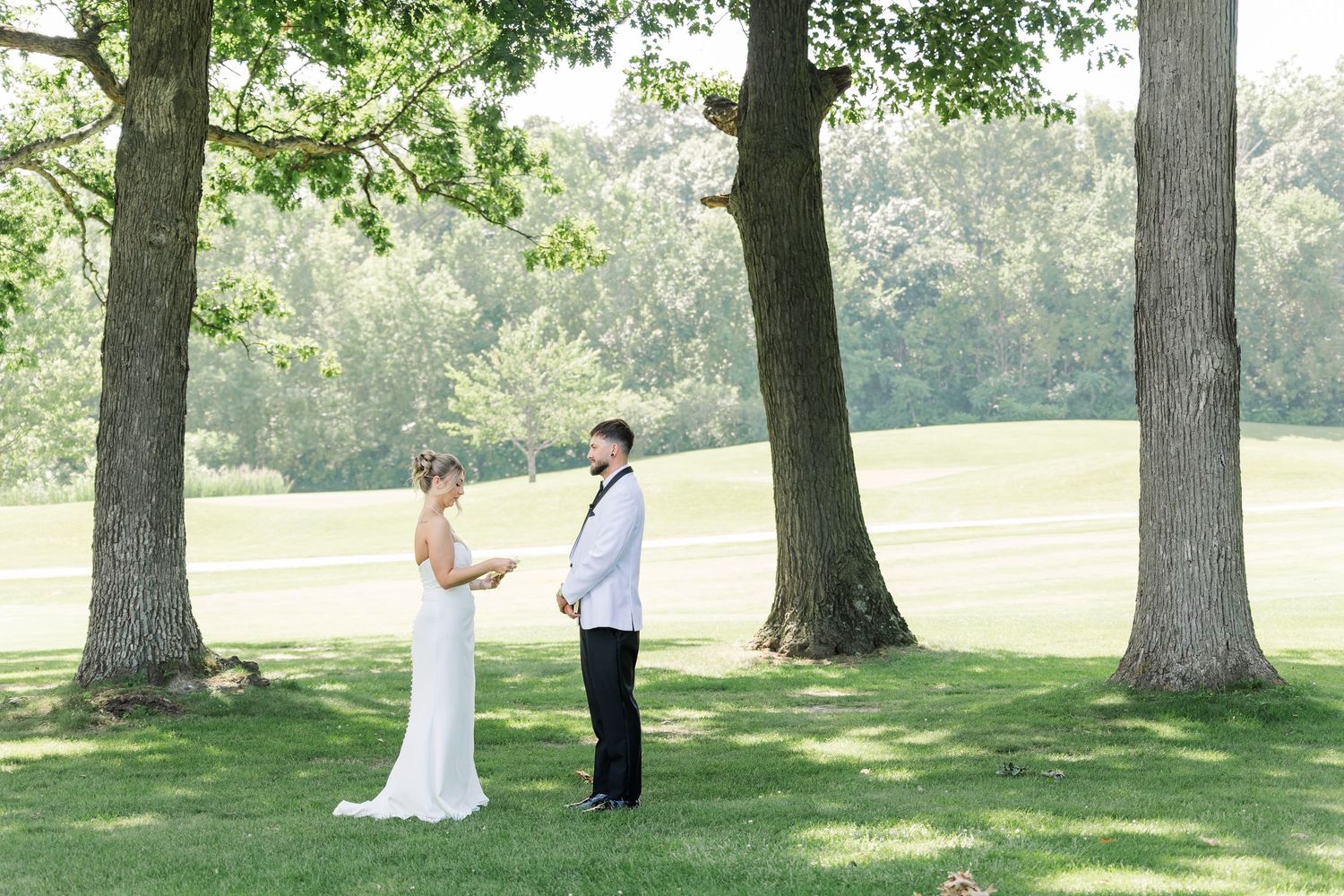 Bride and groom share first look moment standing between two large trees on golf course.