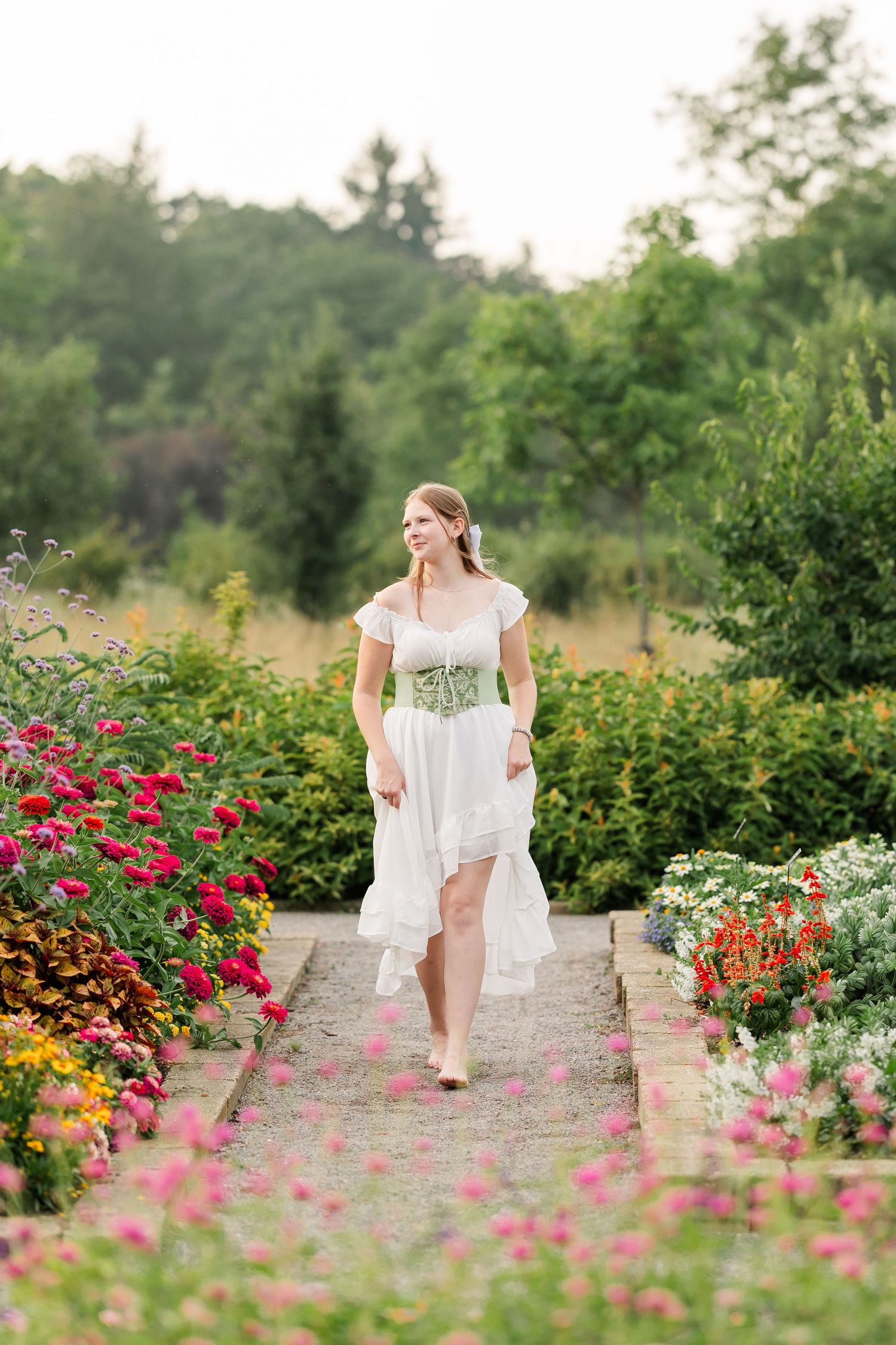 Samantha walks barefoot through a colorful flower garden during her whimsical senior portraits at Cantigny Park.