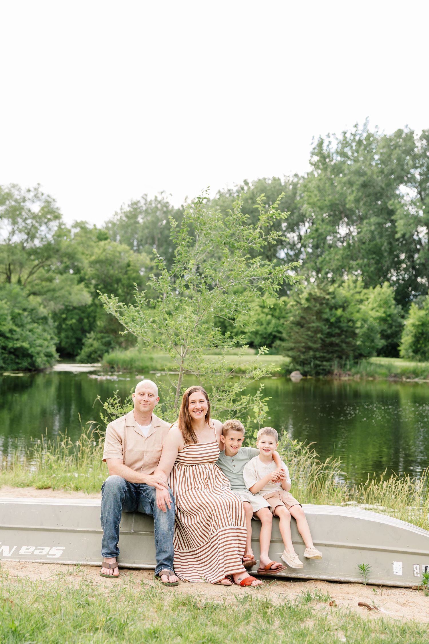 Family of four seated by the lake during a summer portrait session at Shamrock Hills Park in Crystal Lake.