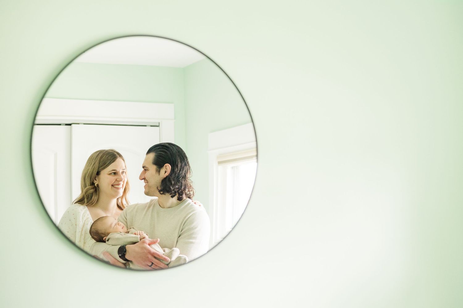 Parents holding their newborn baby reflected in nursery mirror during an in-home lifestyle newborn session in Palatine Illinois