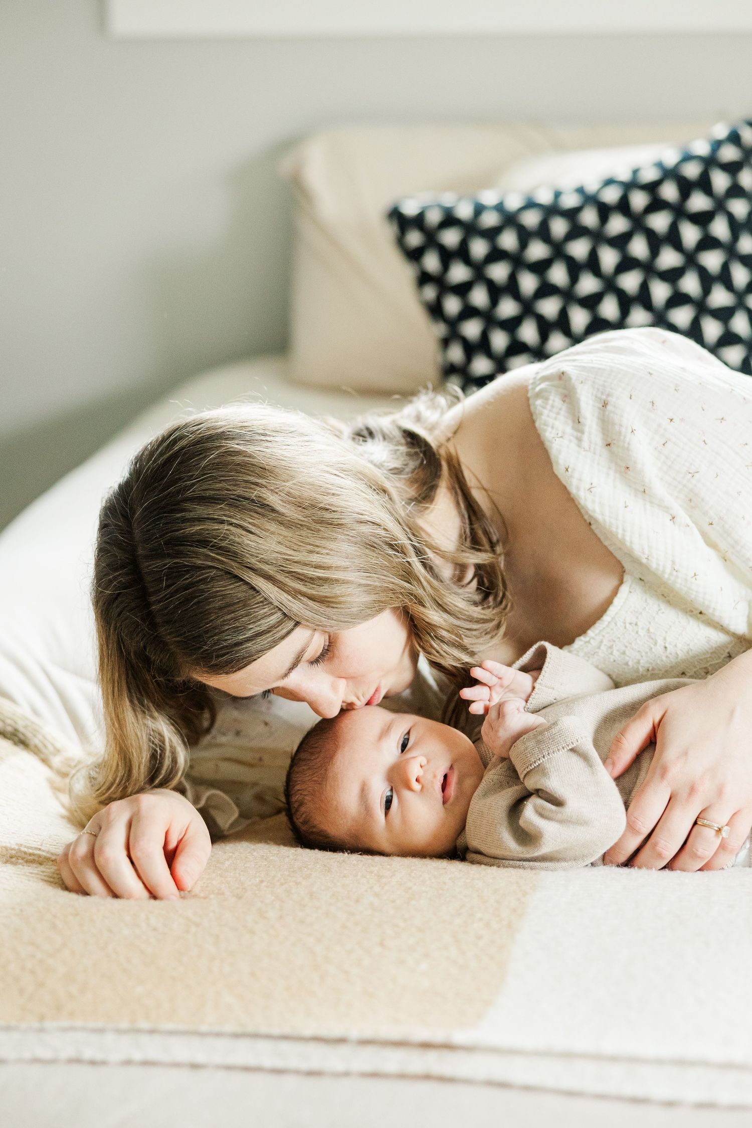 Mother kissing her newborn baby while lying together on a bed during an in-home lifestyle newborn session in Palatine Illinois