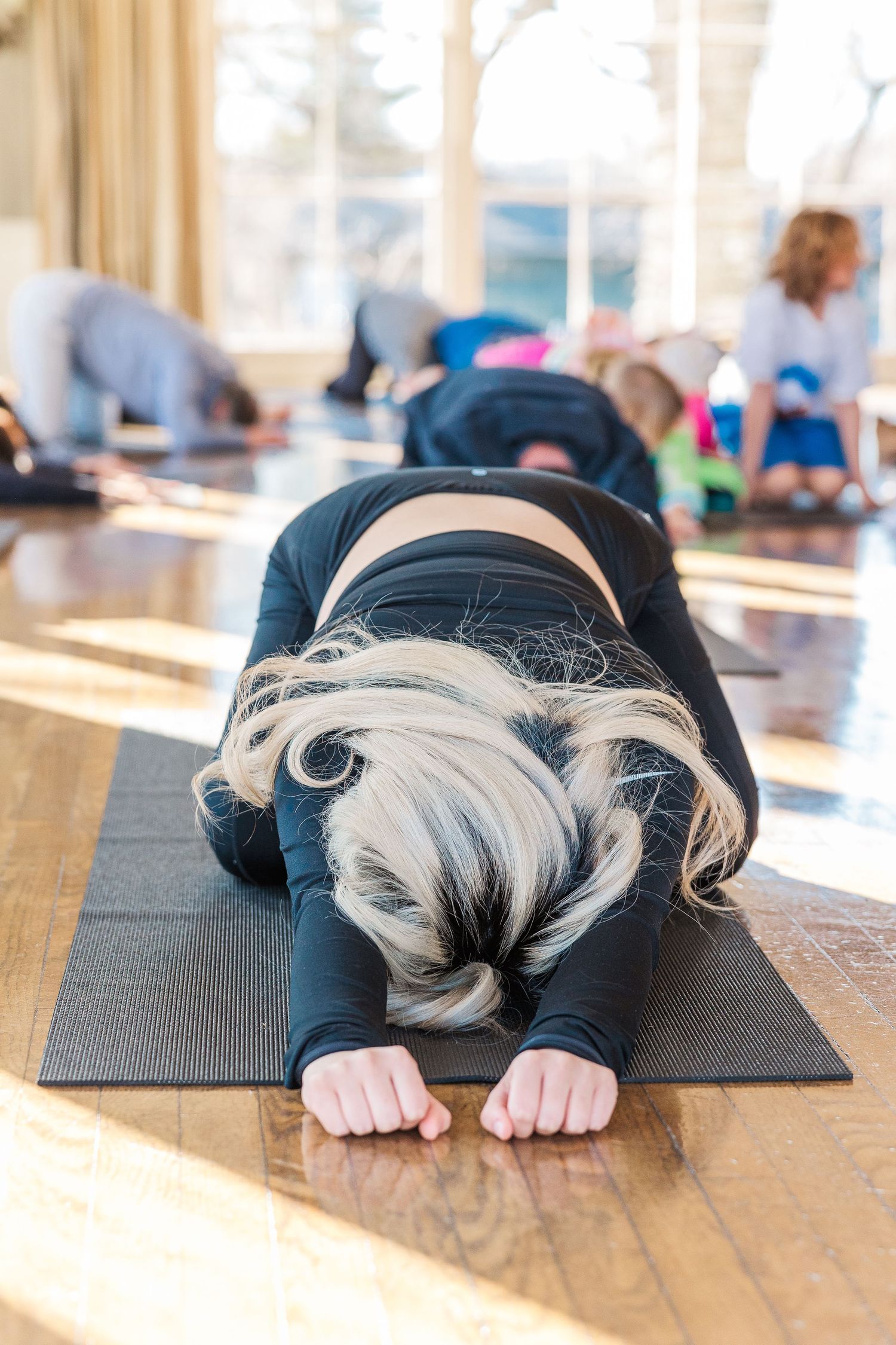 Yoga participant in child's pose on black mat during goat yoga class.