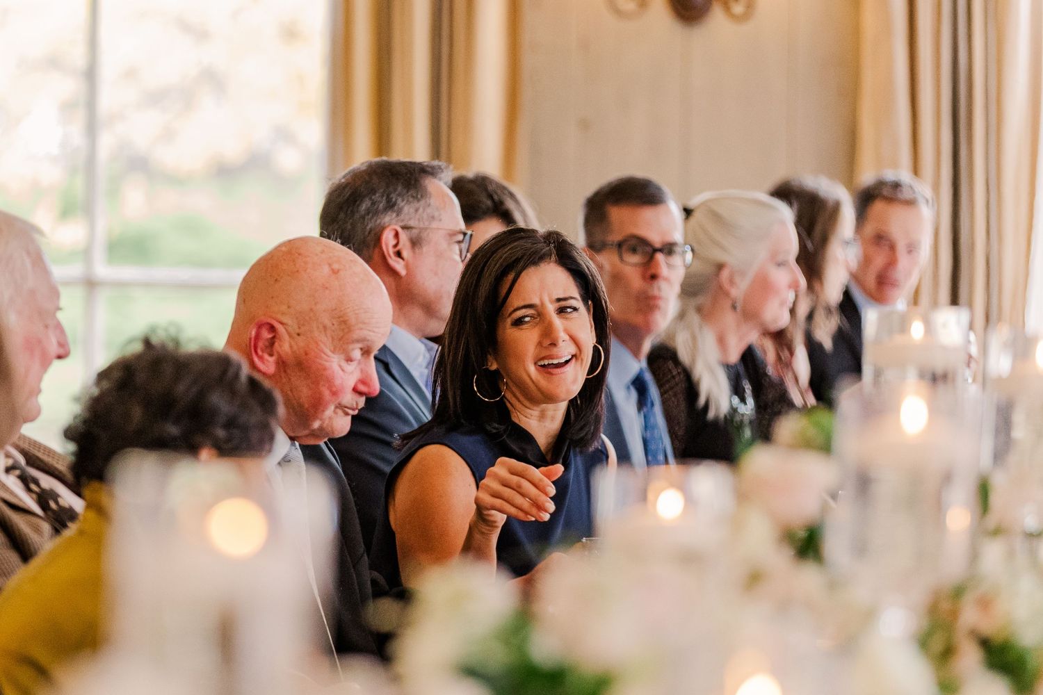 Lively wedding reception scene with guests engaged in animated conversation at decorated dining table.
