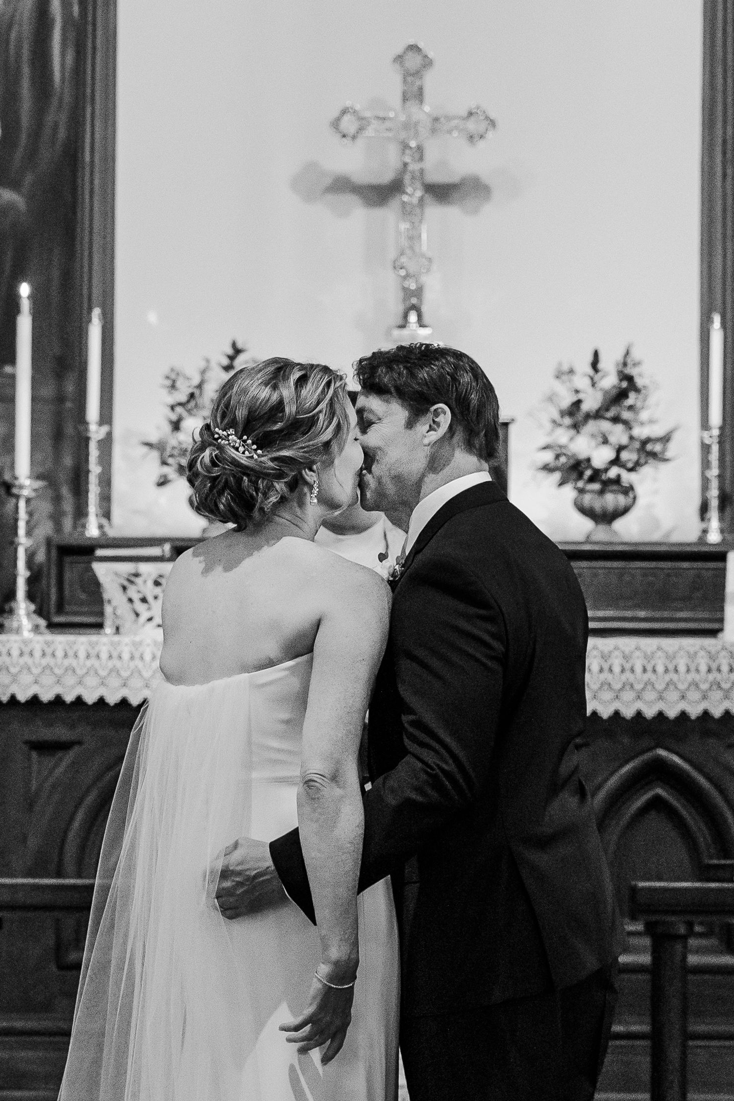 A romantic moment shared during wedding ceremony beneath ornate church cross.