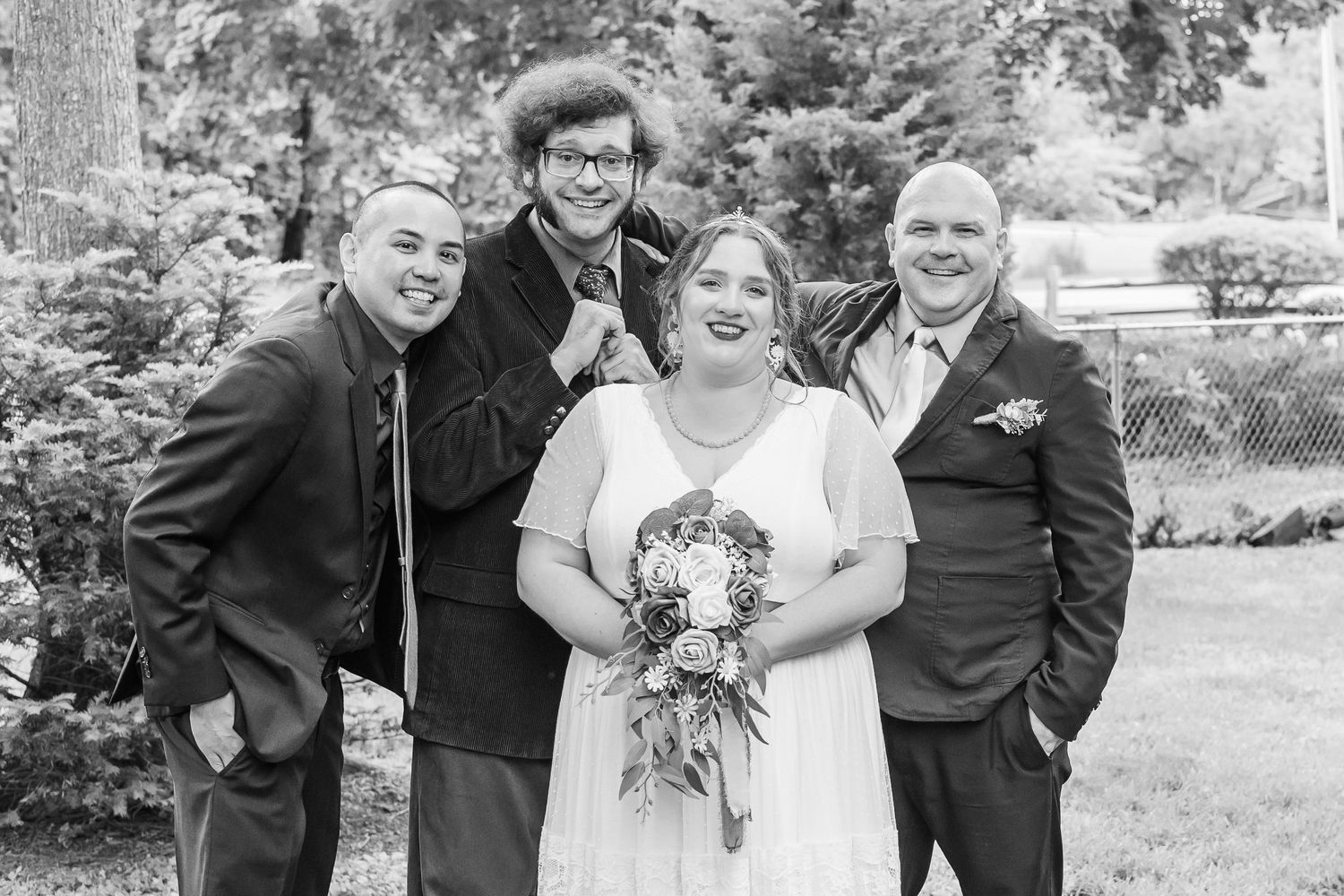 A wedding party poses together in black and white for a casual outdoor portrait.
