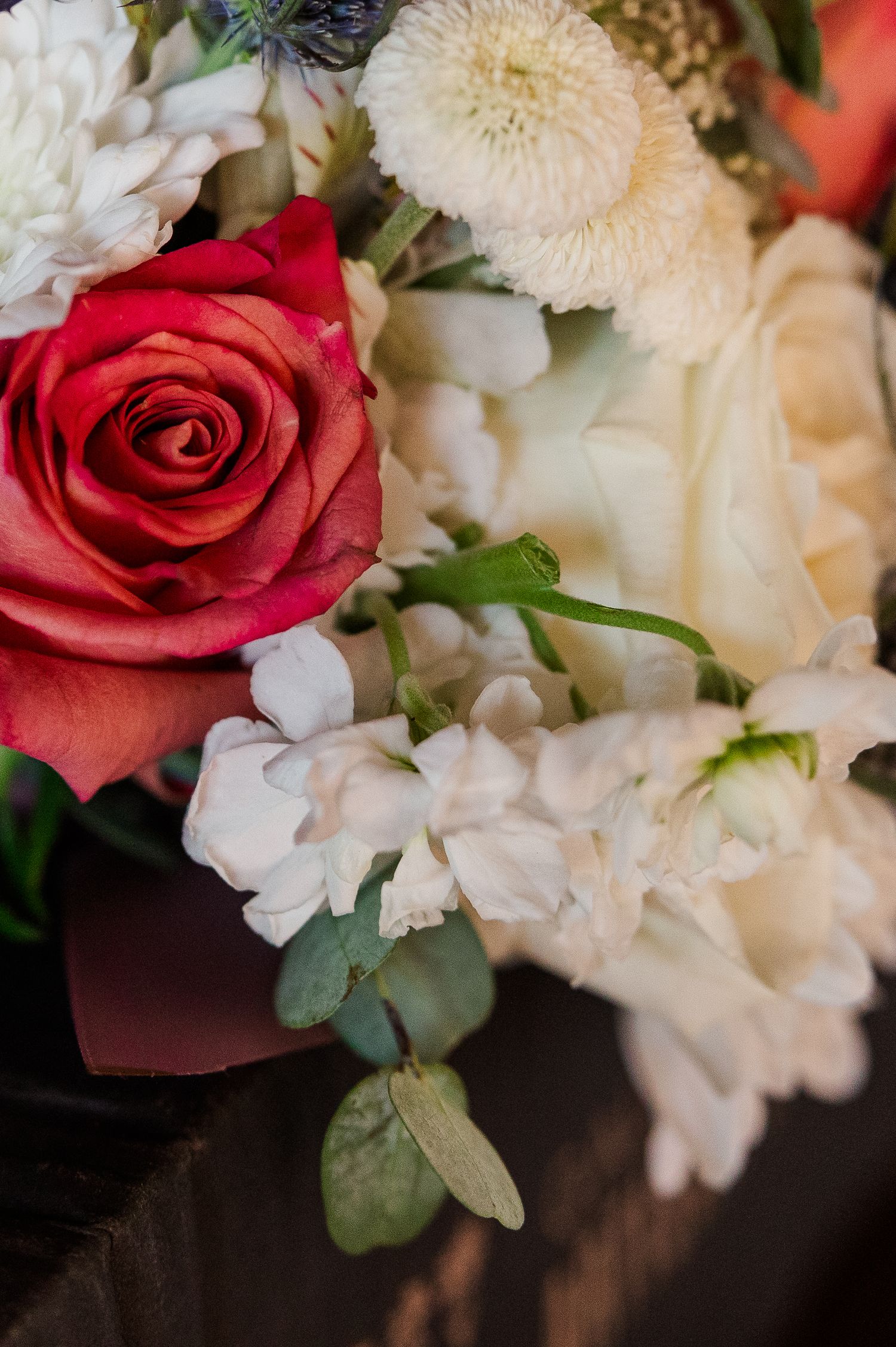Elegant bouquet with coral red roses and white flowers arranged with green foliage.