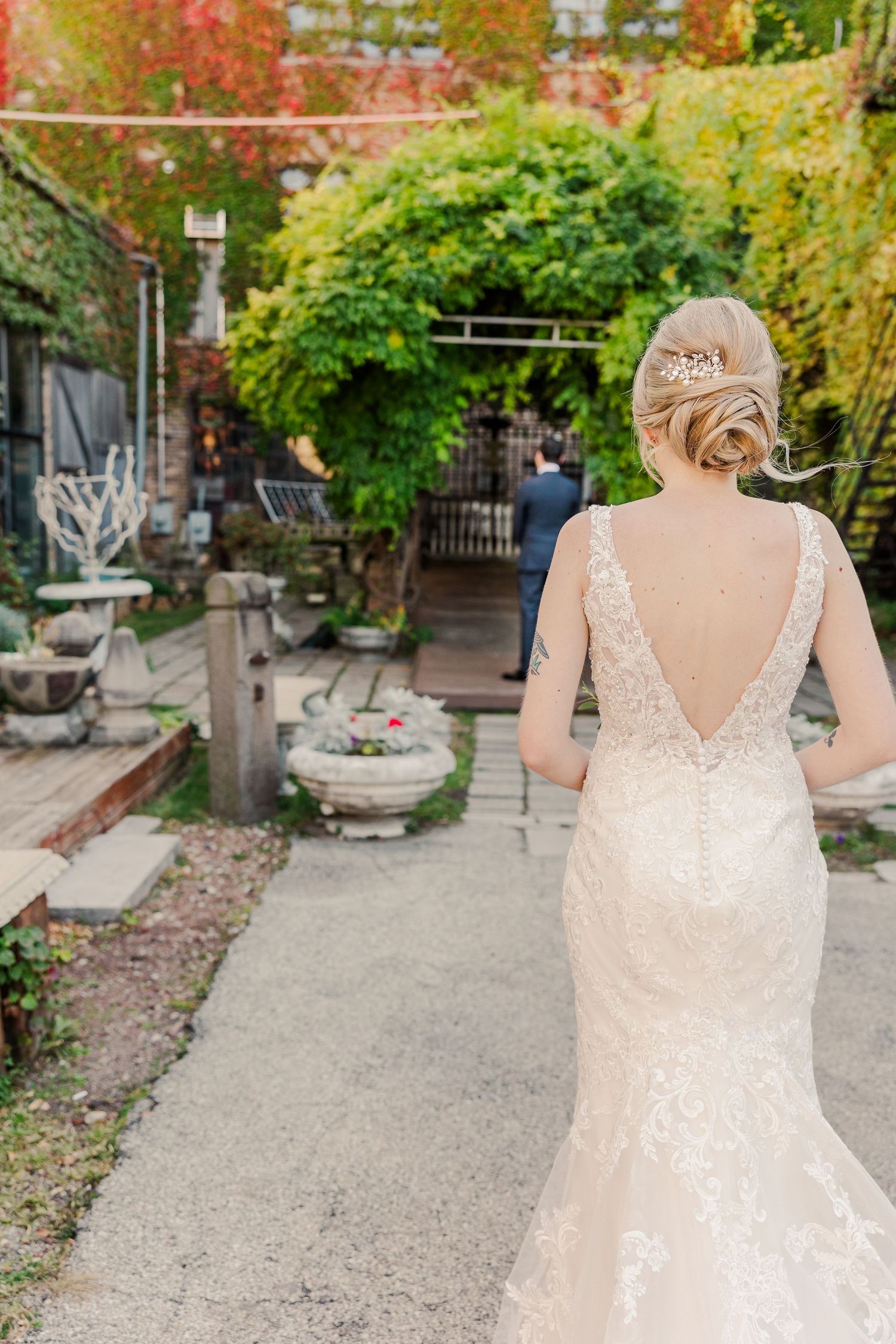 Back view of a bride in a lace wedding dress with deep V-back in a garden setting.
