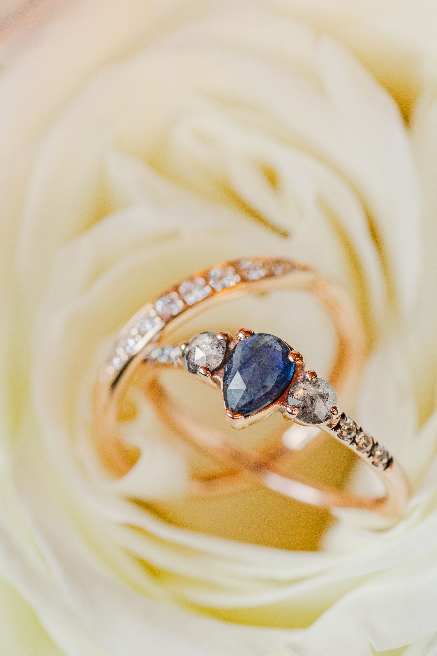 Close-up of a delicate sapphire and diamond ring set against white rose petals.