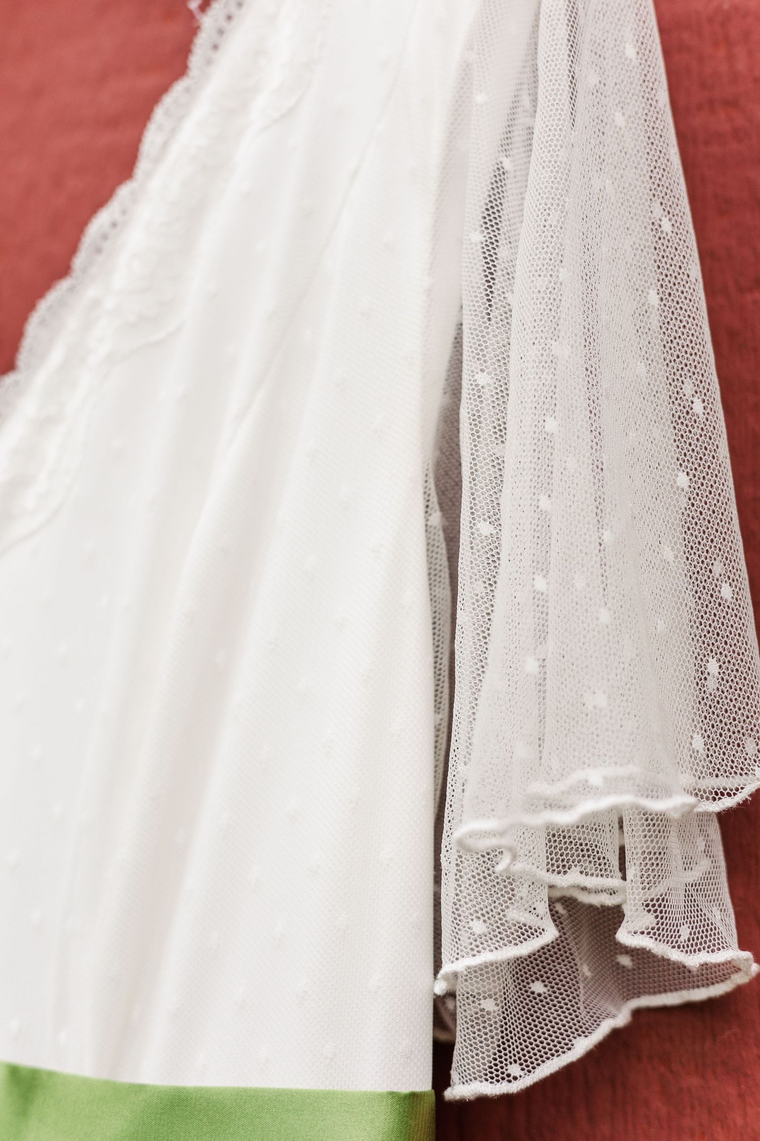 Detail of white tulle wedding dress fabric with lace trim against red background.