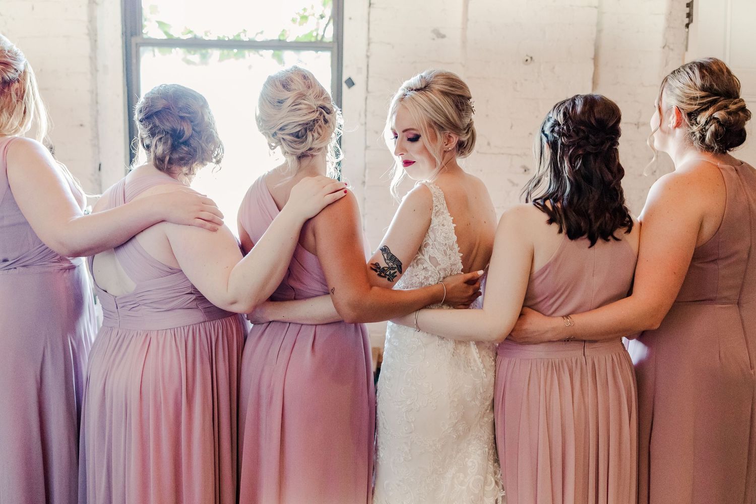Intimate bridal party moment captured in soft lighting by vintage window.