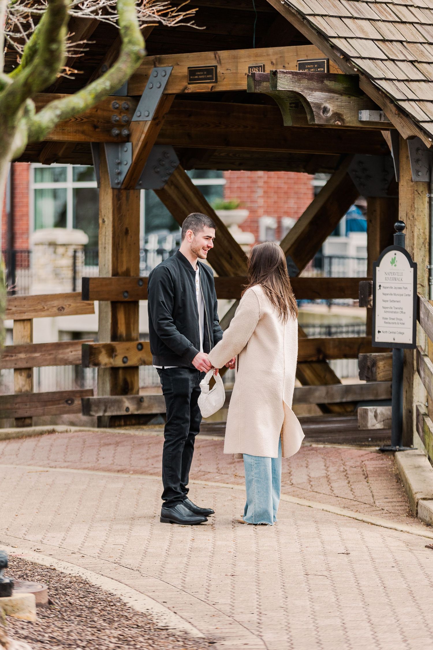 A couple stands beneath a rustic wooden gazebo on a brick path.