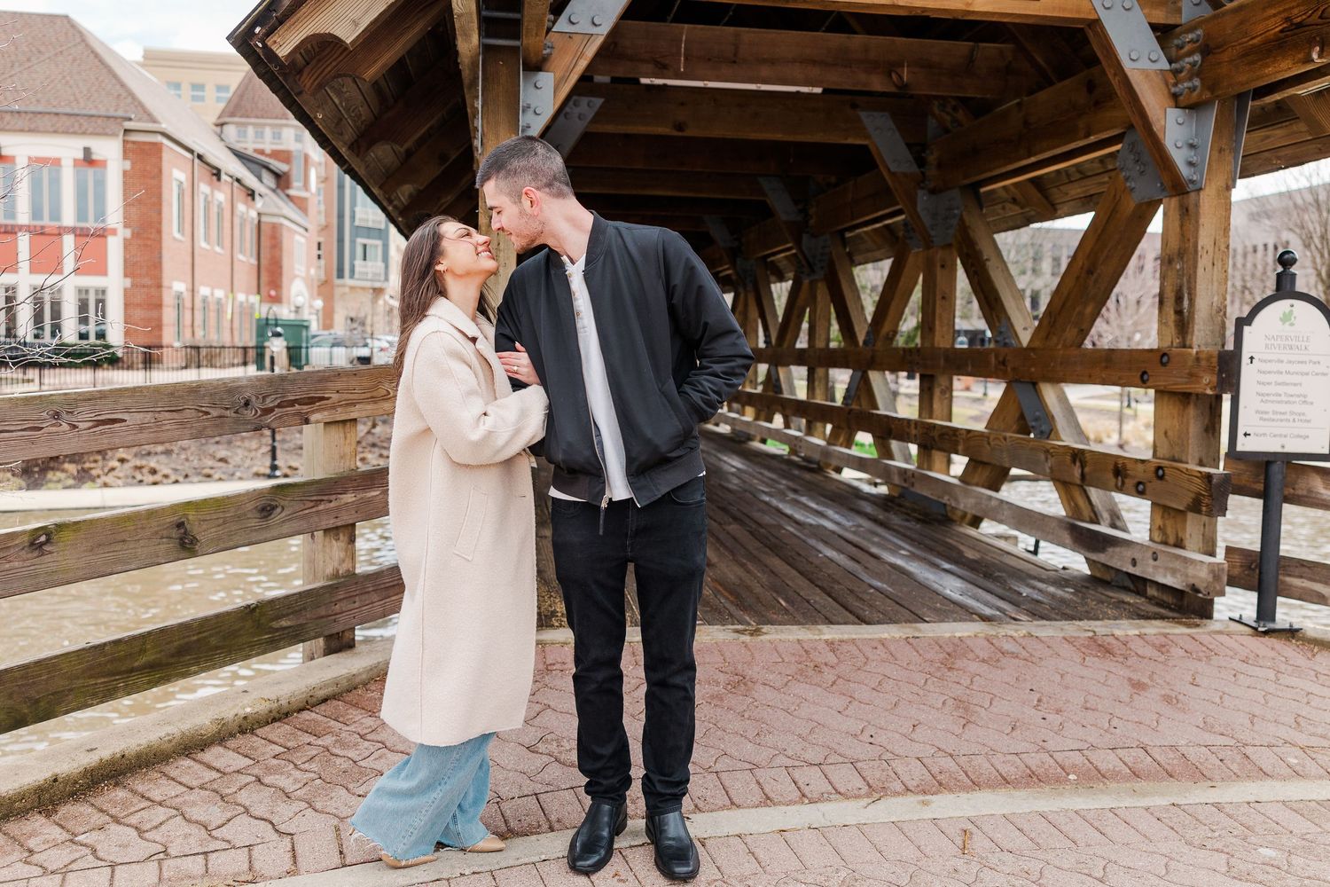 A couple in casual winter attire sharing a tender moment on a covered bridge.