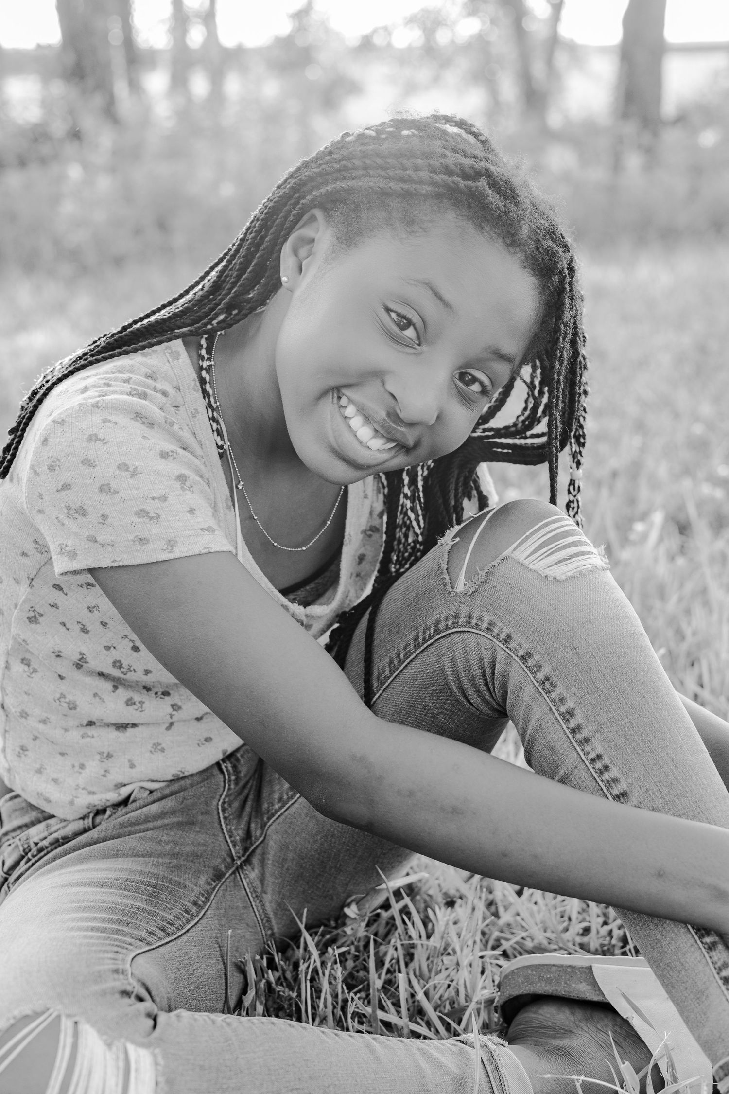 Black and white portrait of someone with braids sitting outdoors and smiling.