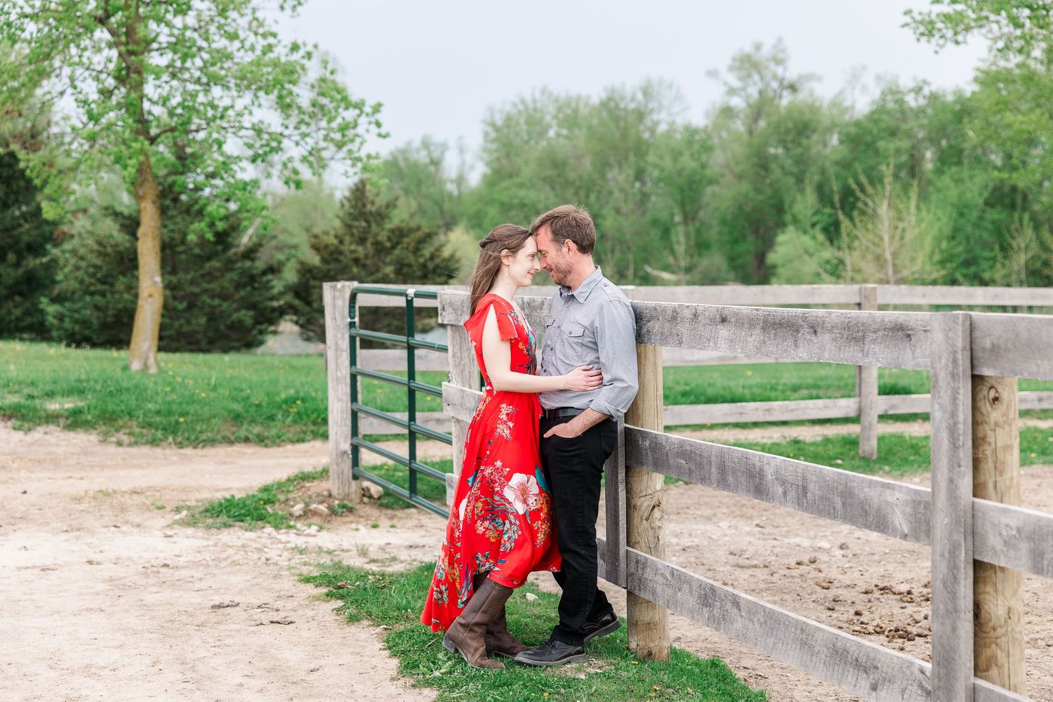 A romantic couple embraces by a wooden fence on a spring day while wearing casual and formal attire.