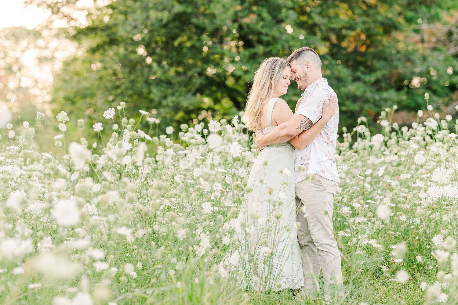 Romantic couple embracing in a meadow of white wildflowers during golden hour.