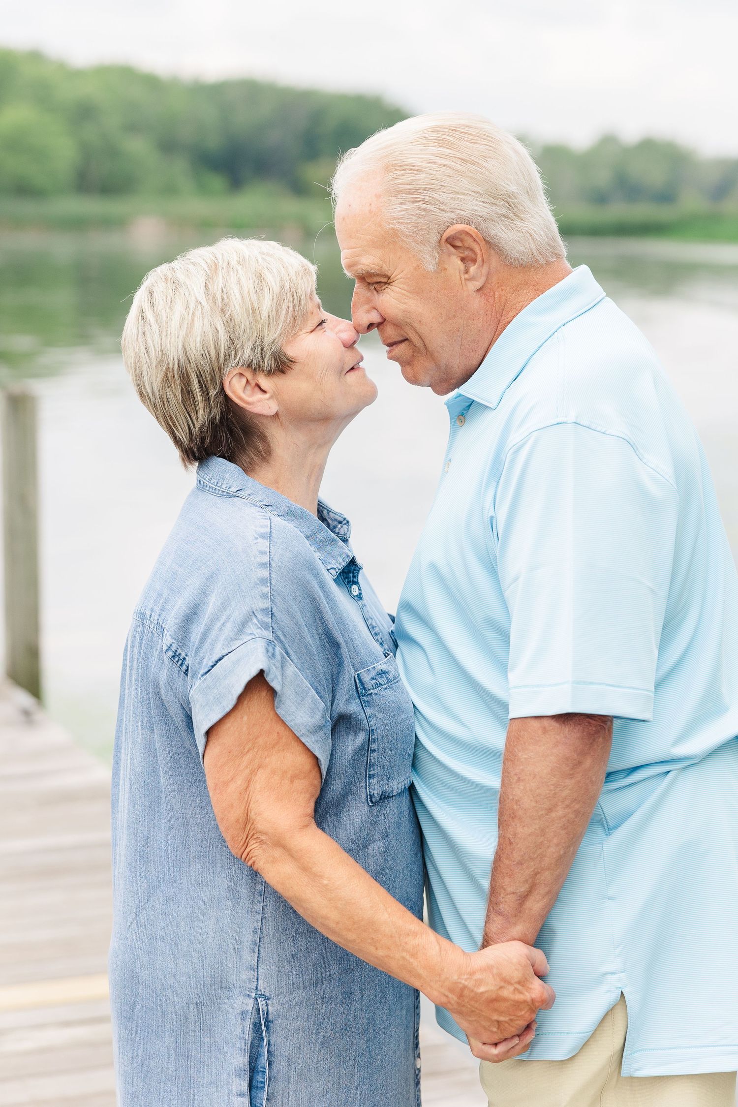 An intimate moment between a couple in casual attire standing on a dock by the water.