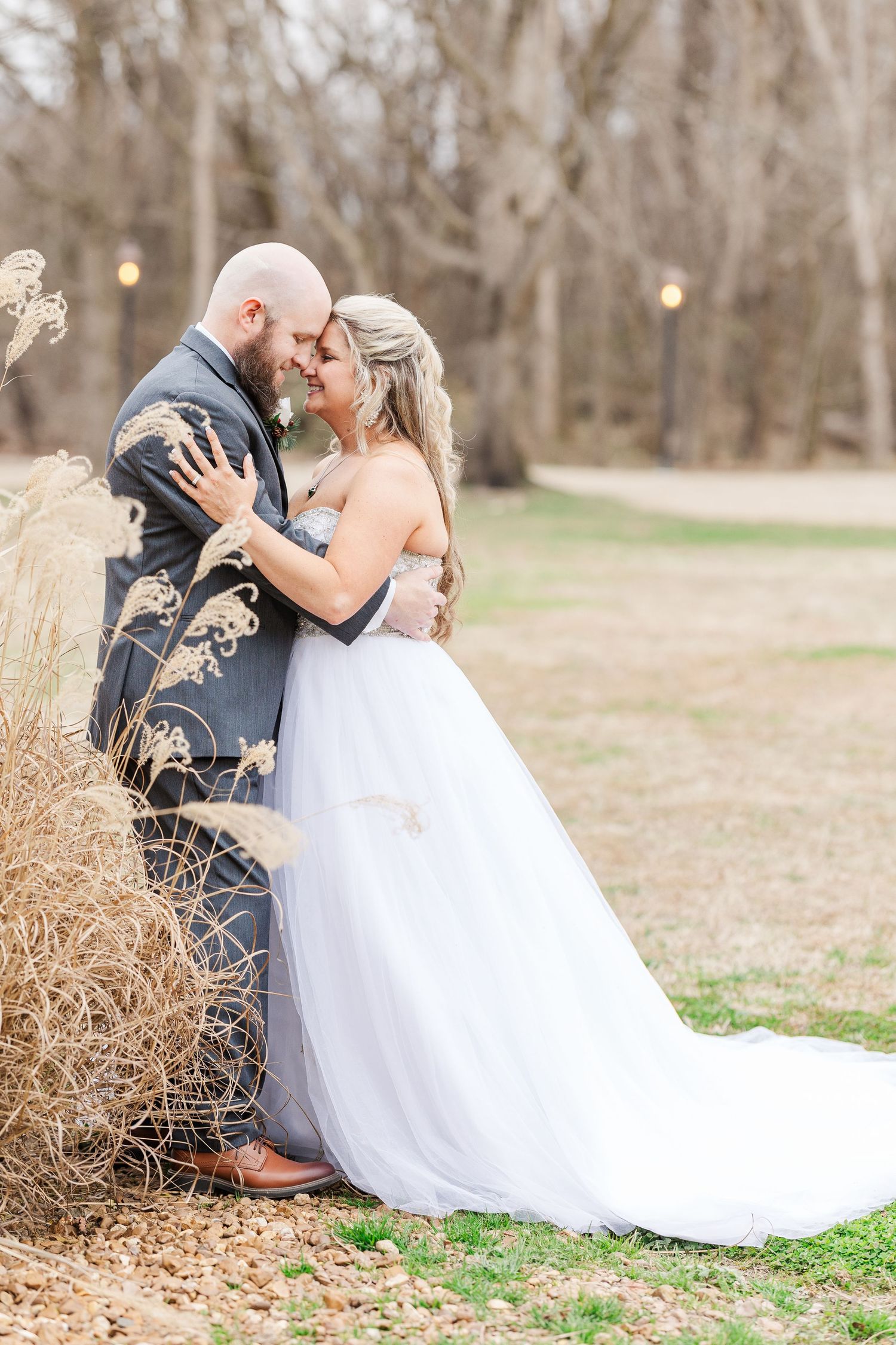 A romantic wedding couple embraces among tall dried grasses in a natural outdoor setting.