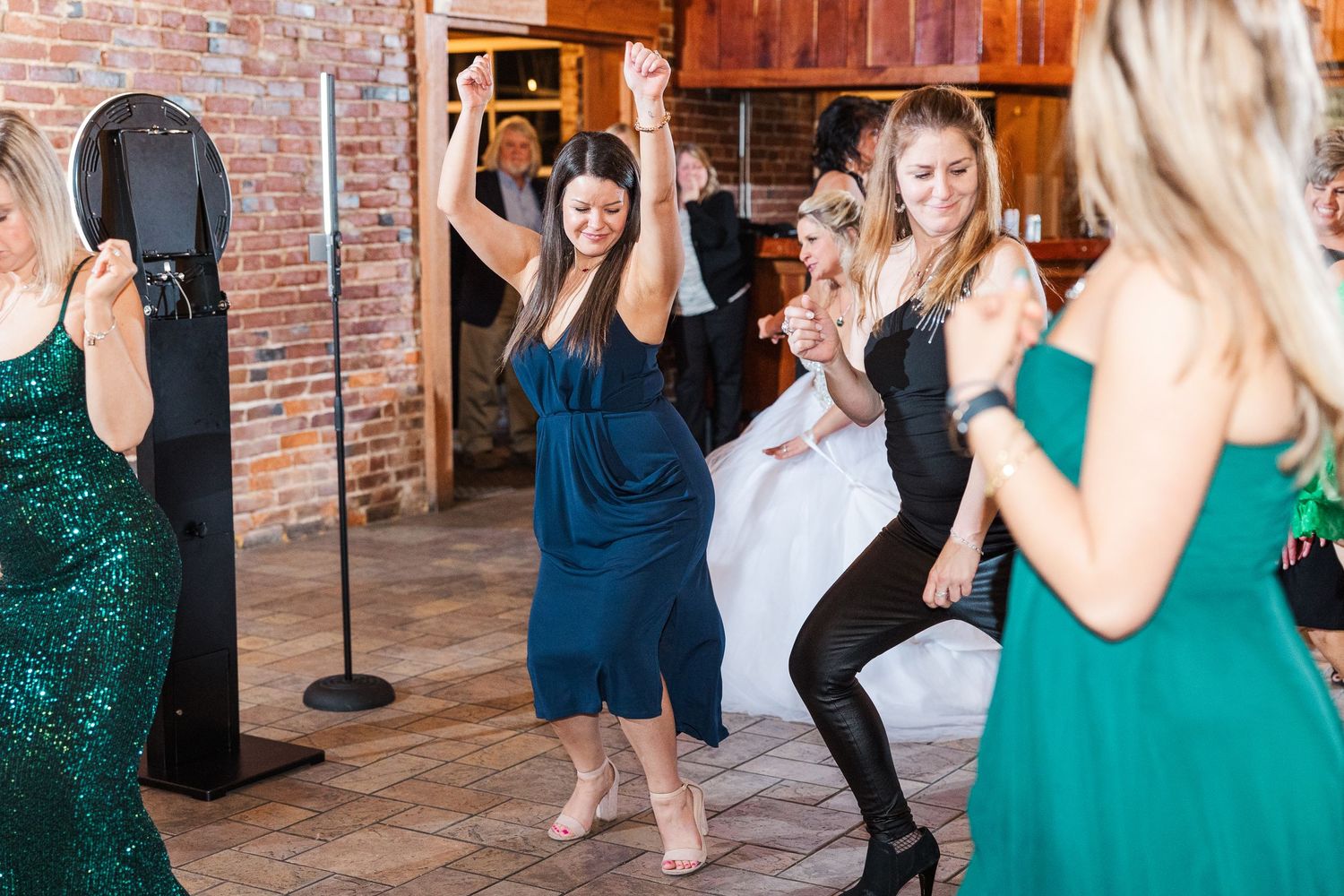 Wedding reception guests dancing and celebrating on the dance floor in a brick-walled venue.