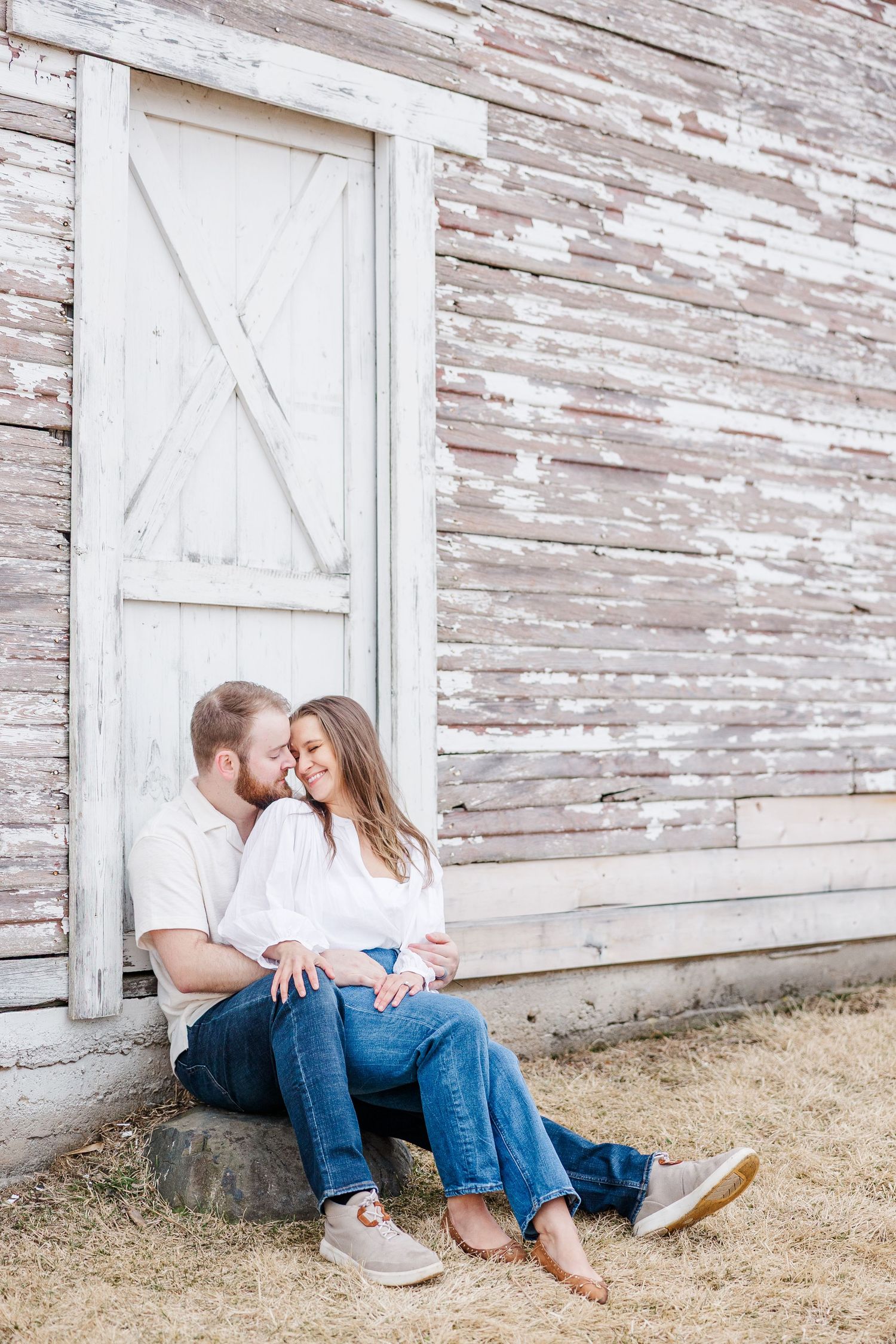 Couple sitting by barn door during pregnancy announcement photos in Cary, Illinois