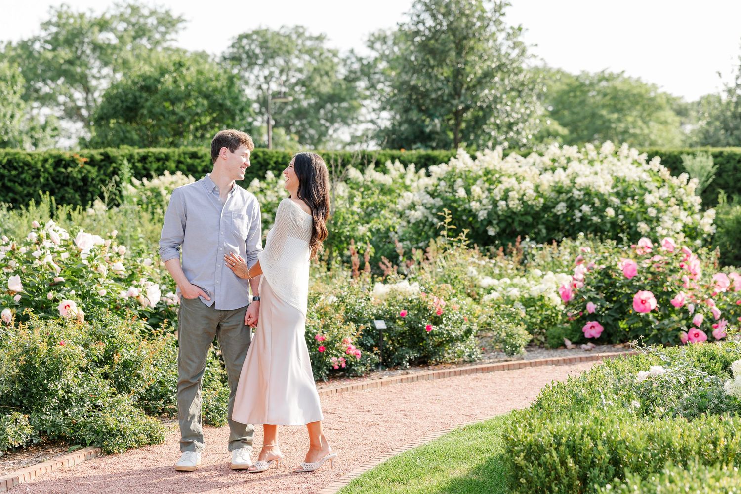Newly engaged Alysia and Jack stand together beside the blooming rose garden.