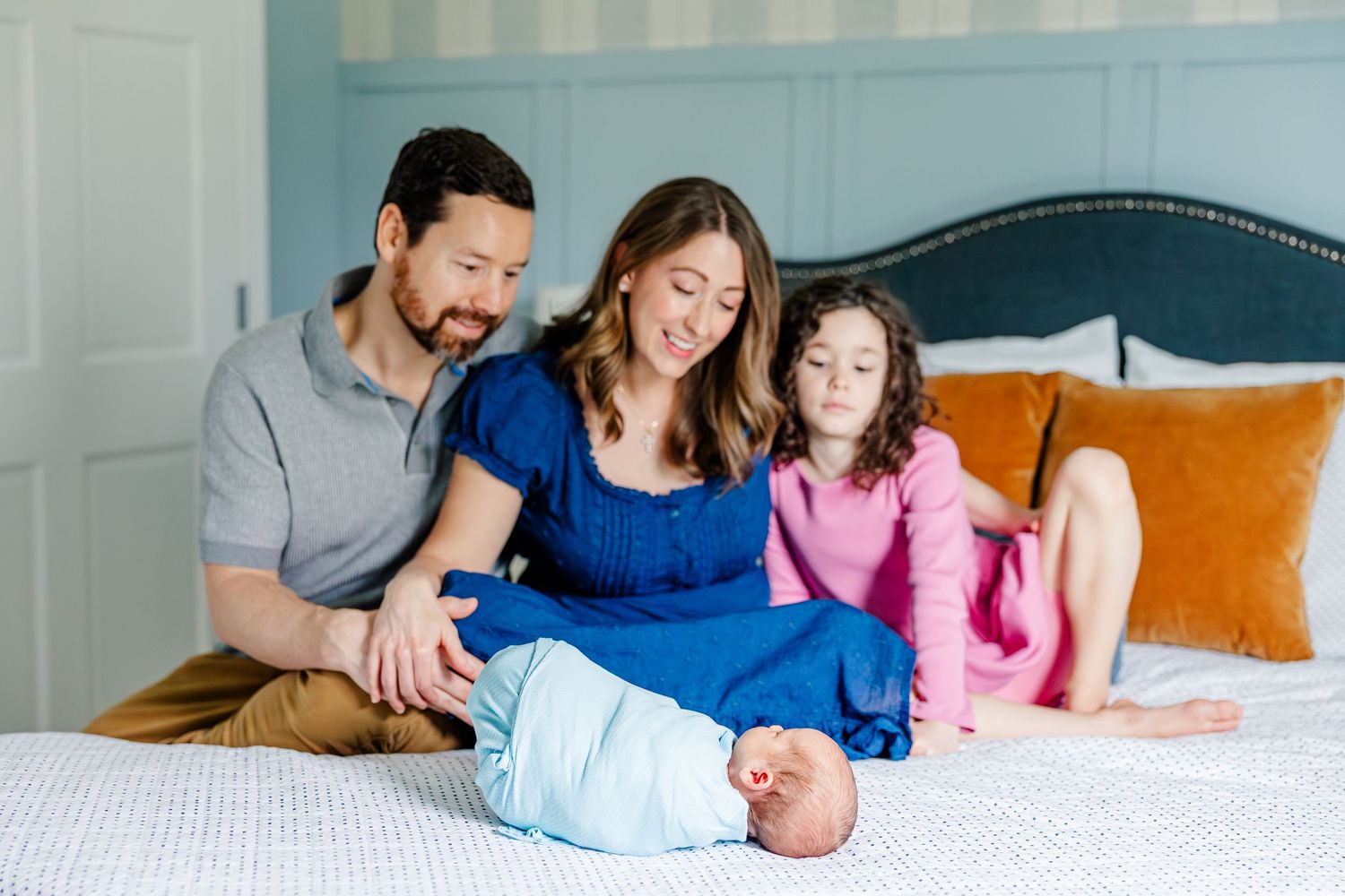 Parents and daughter with newborn on bed during lifestyle newborn session in Crystal Lake, Illinois