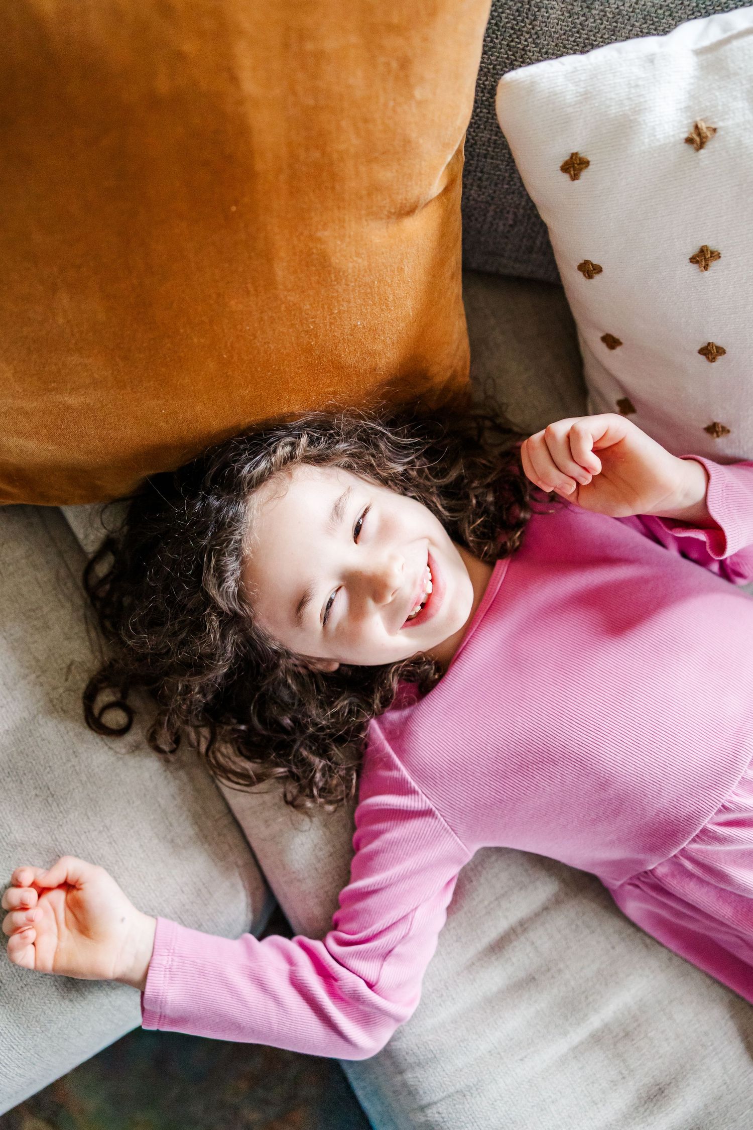 Big sister rests on couch during bright lifestyle newborn session in Crystal Lake, Illinois