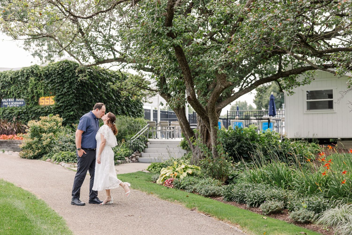Couple walking along a garden path lined with colorful flowers and trees at an outdoor venue.